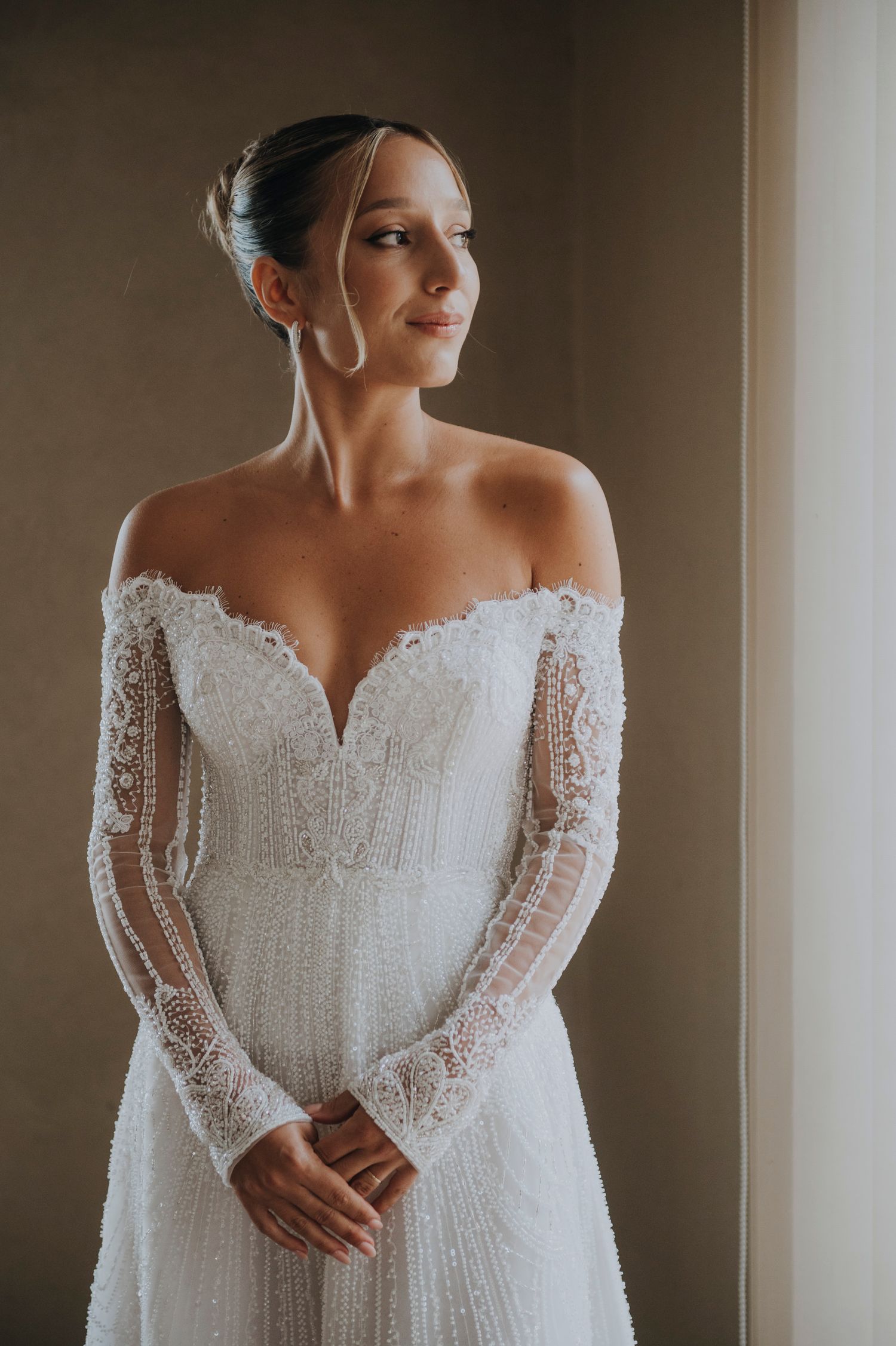 Bride in off-shoulder lace wedding gown with long sleeves gazing softly to the side in natural light.