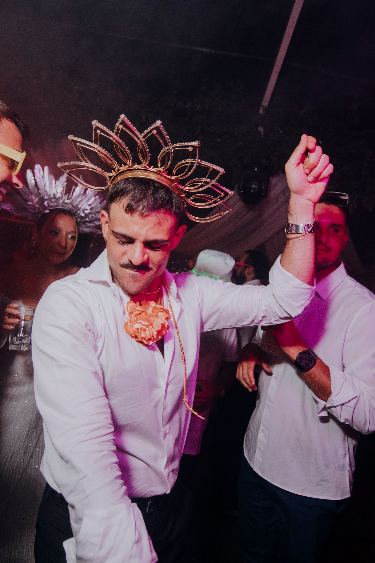 Groom dances joyfully wearing a decorative gold crown and fake mustache at a lively wedding reception party.