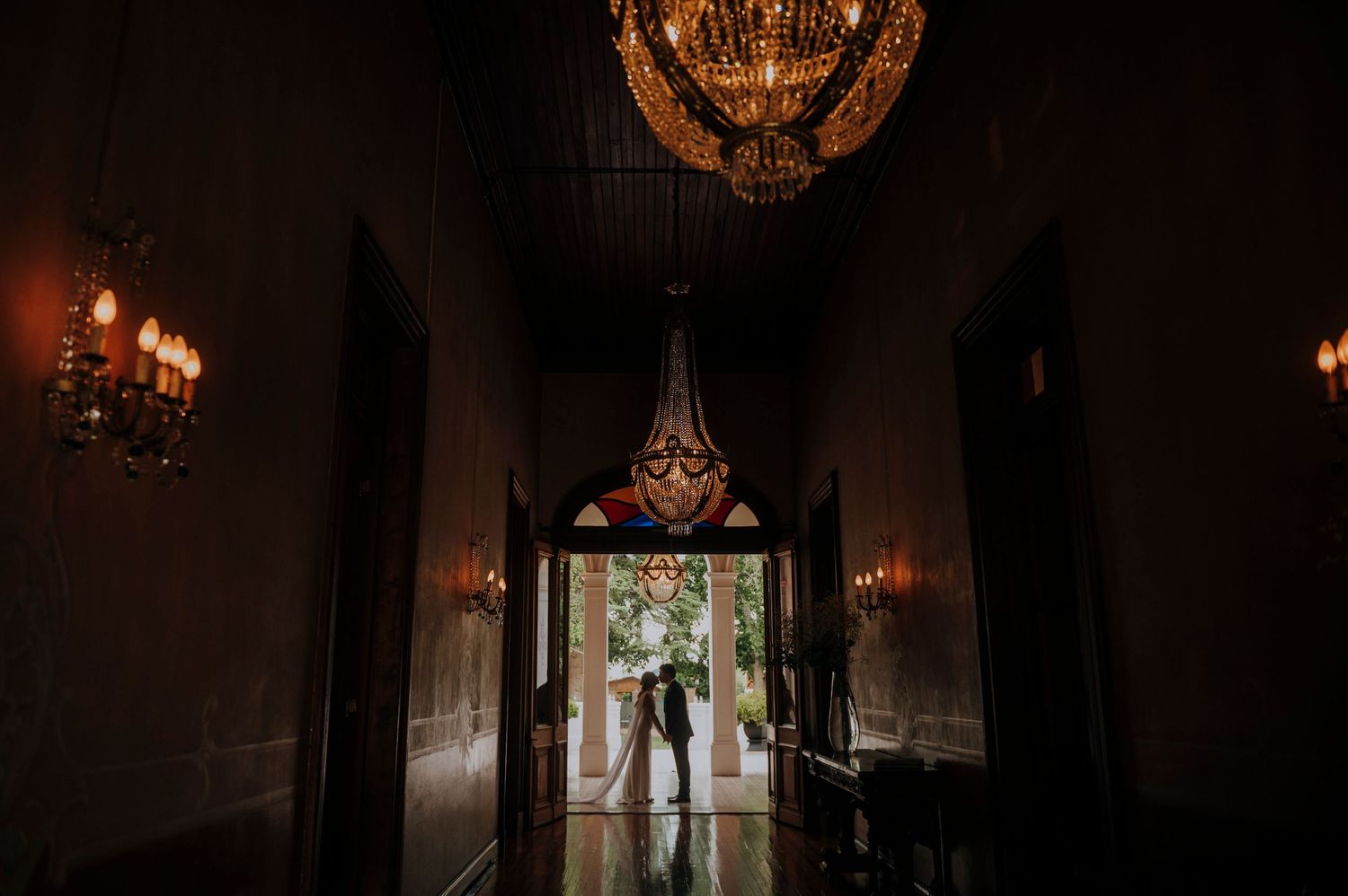 Couple embracing in a dark elegant hallway with ornate crystal chandeliers and warm candlelight at a wedding venue.