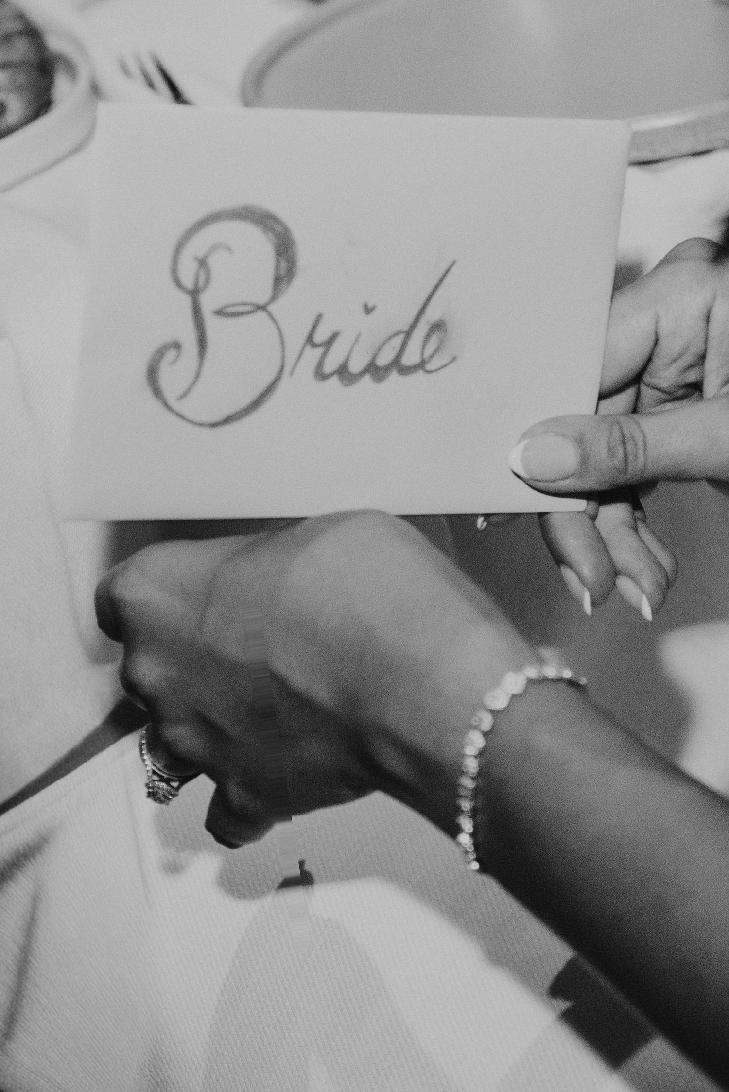 Black and white photo of hands holding a bride place card with pearl bracelet.