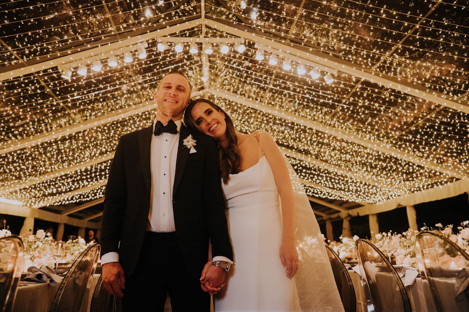 Couple posing under stunning fairy light canopy at elegant wedding reception venue.