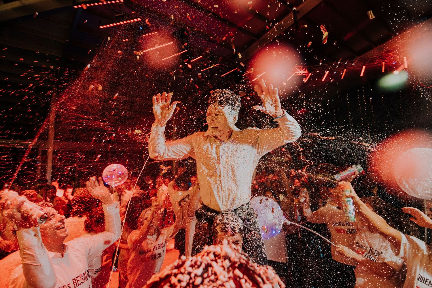 Groom celebrates joyfully amid confetti and cheering guests on the wedding dance floor.