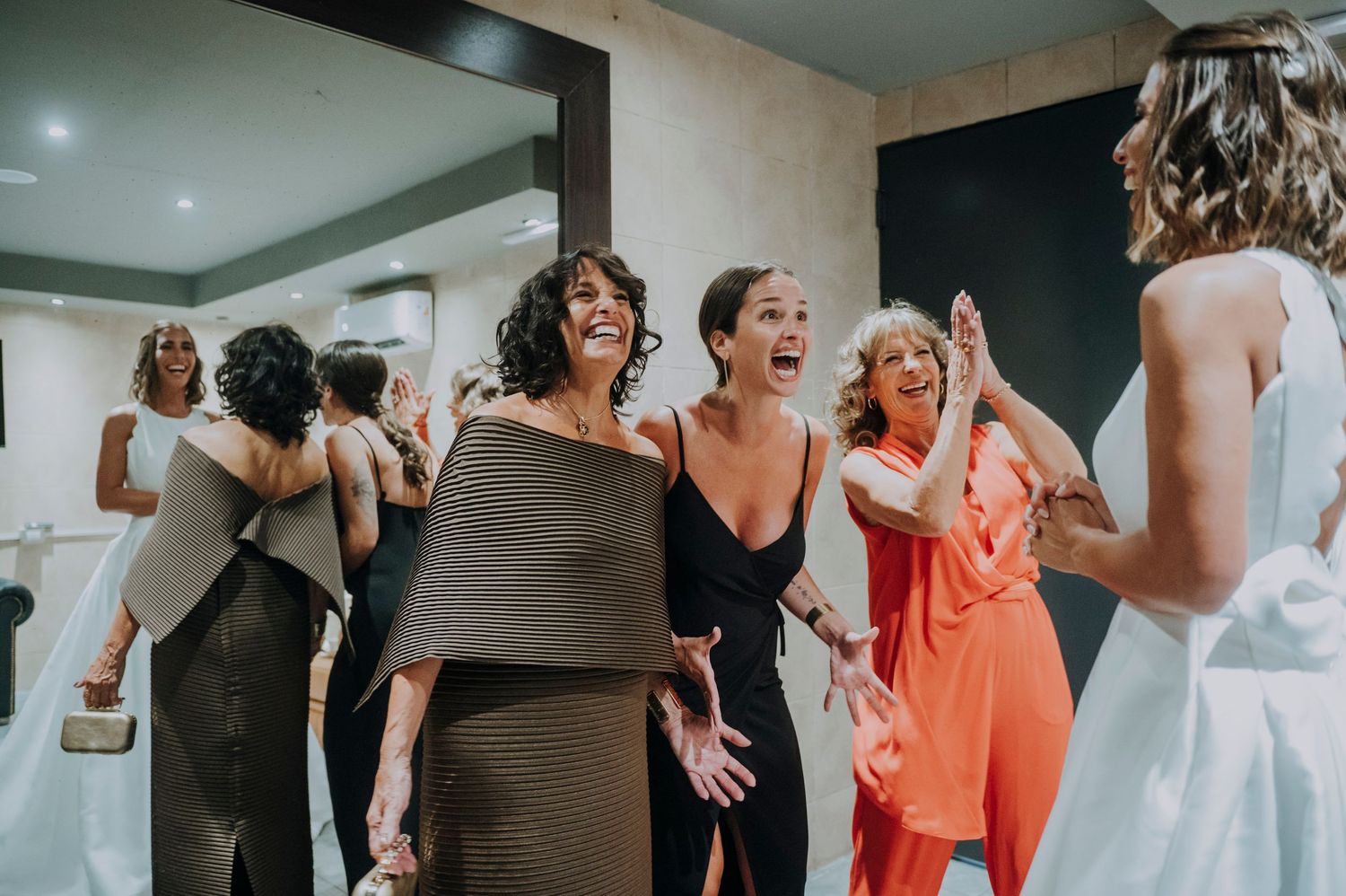 Excited bridesmaids in elegant dresses react with joy upon seeing the bride during wedding preparations.