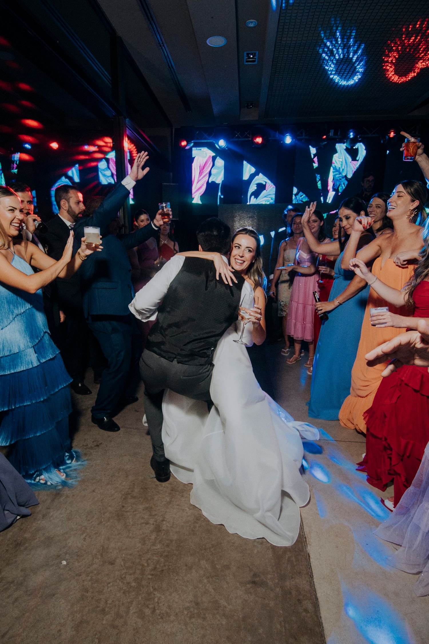 Groom lifts bride on a crowded dance floor surrounded by celebrating guests at a vibrant wedding party.