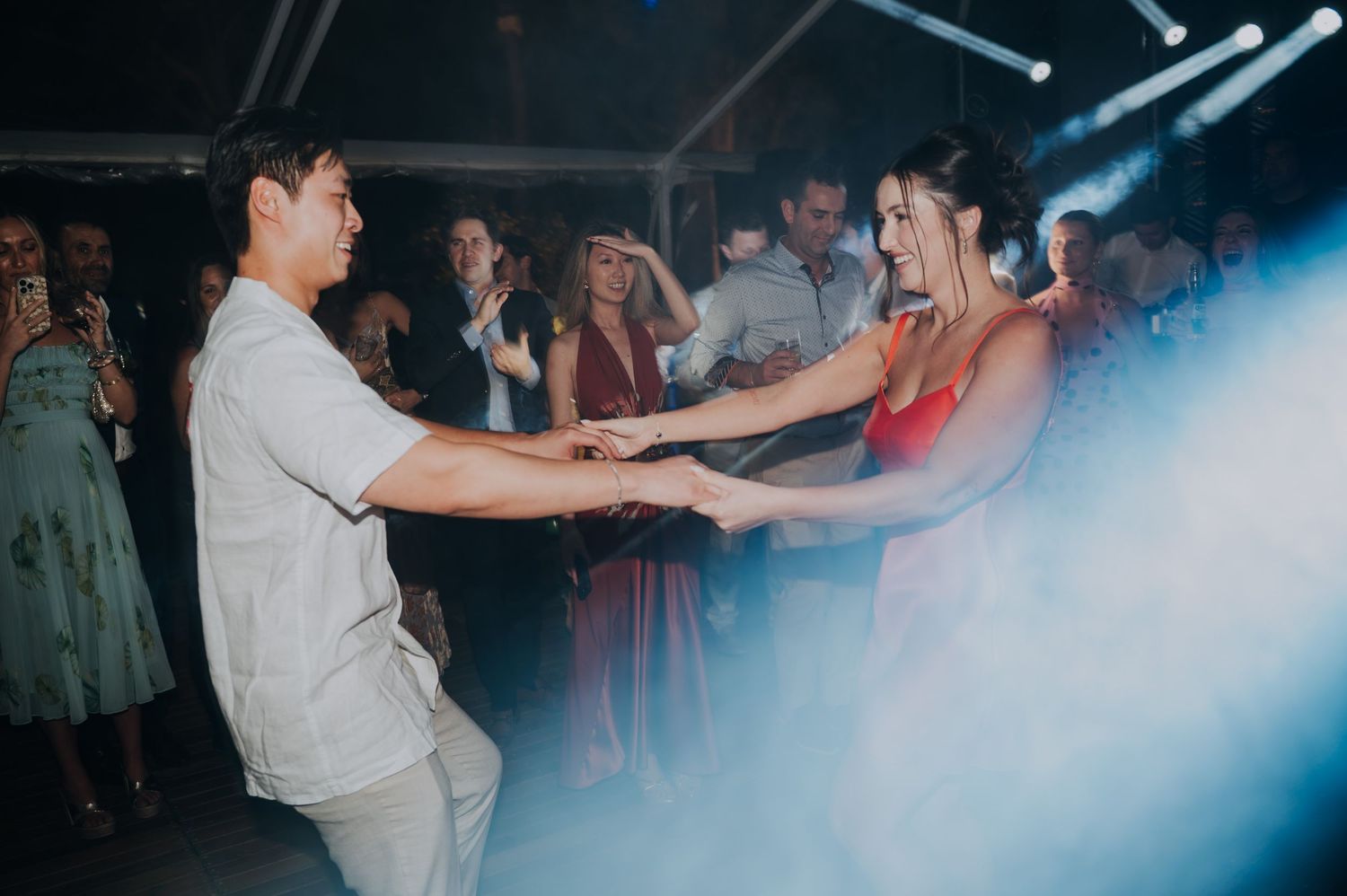 Couple dancing together on a foggy dance floor at a wedding reception with guests watching in the background.