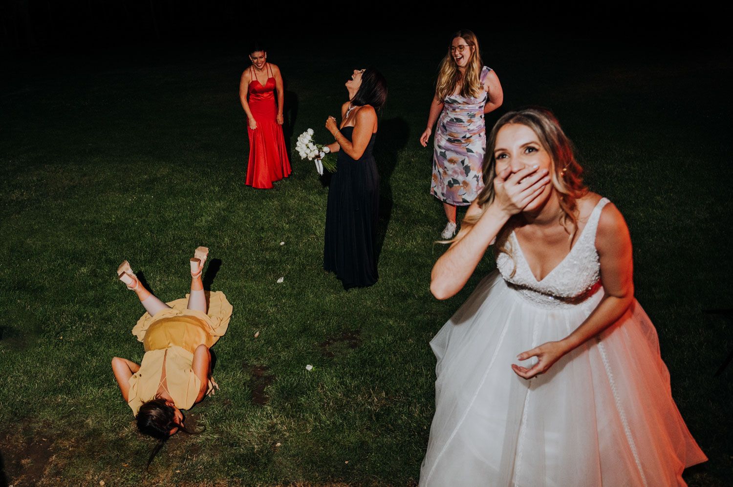 Bride covers mouth in shock as bridesmaid falls on grass at wedding reception in Mendoza, Argentina.
