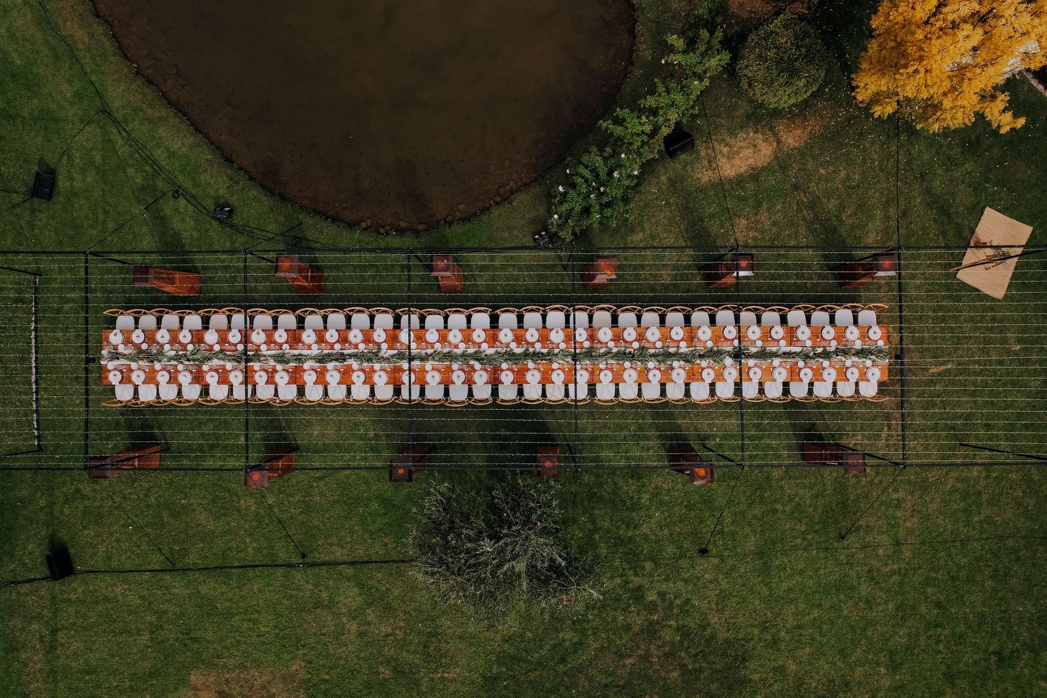 Aerial view of long outdoor wedding reception table set with white and orange arrangements.
