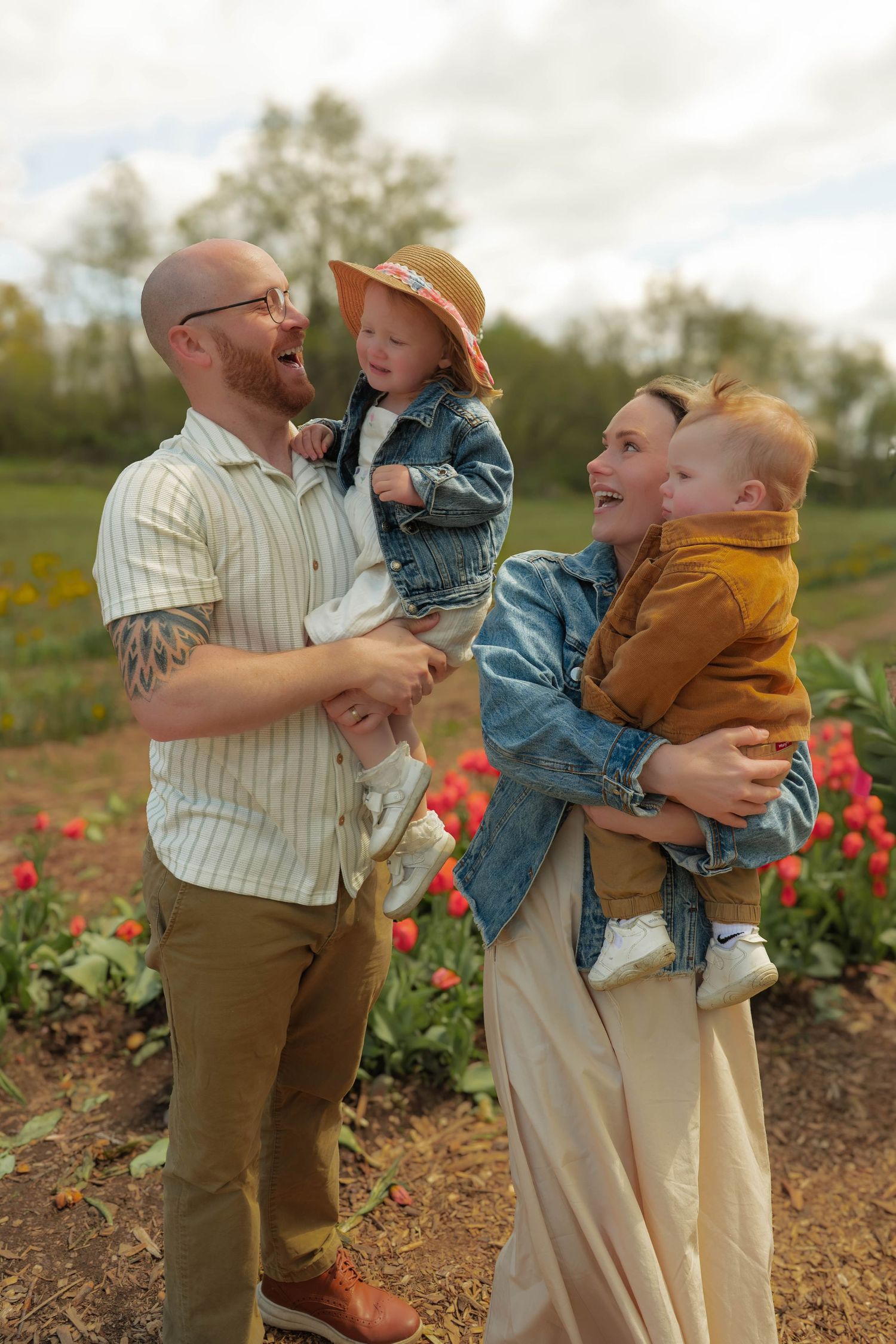 Happy family laughing together while holding two young children near tulip garden.