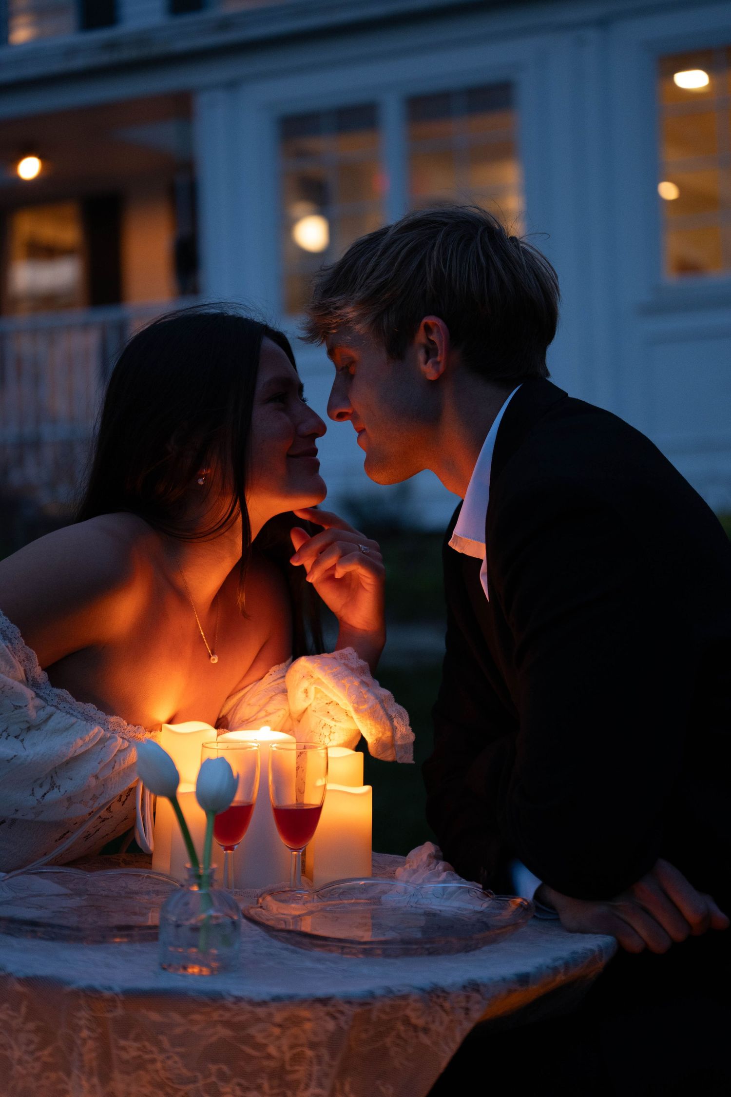 Romantic couple gazes at each other by candlelight at an outdoor table with wine glasses.