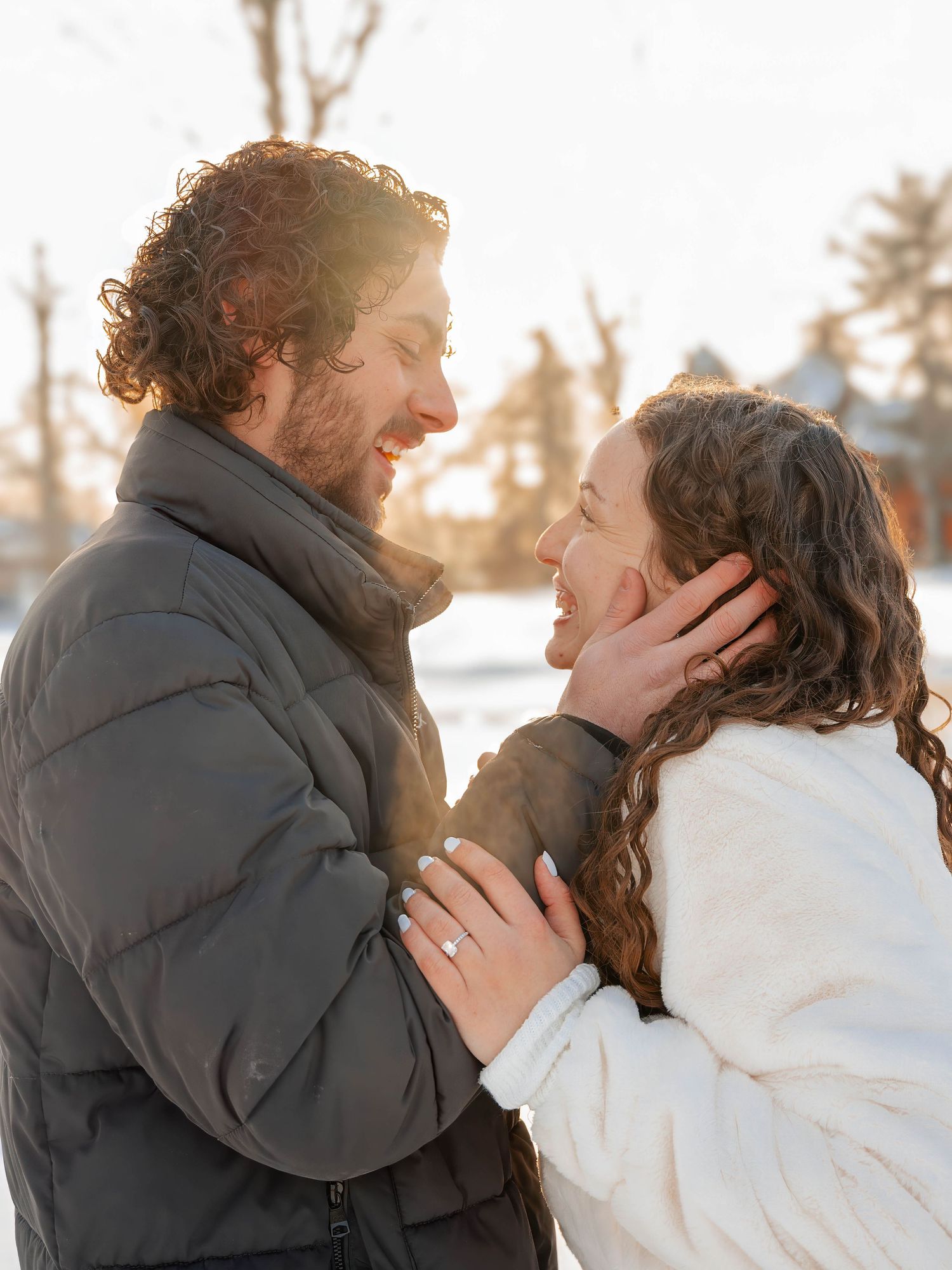 Joyful newly engaged couple smiling at each other in golden winter sunlight outdoors.