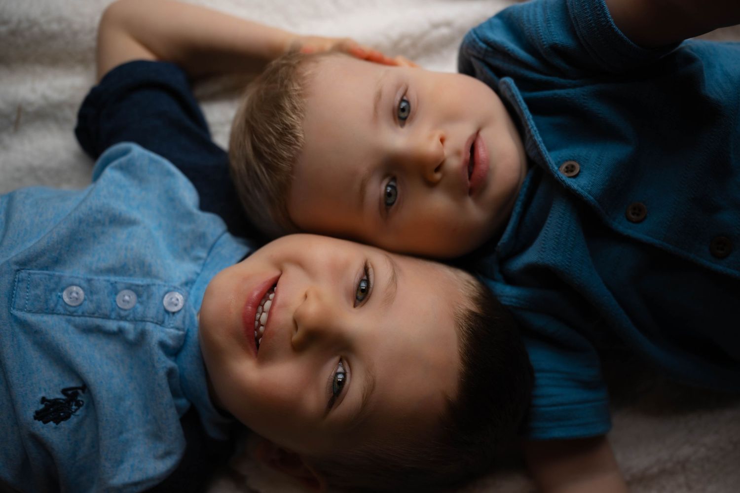Two young brothers lying head to head on a white surface, smiling at the camera.