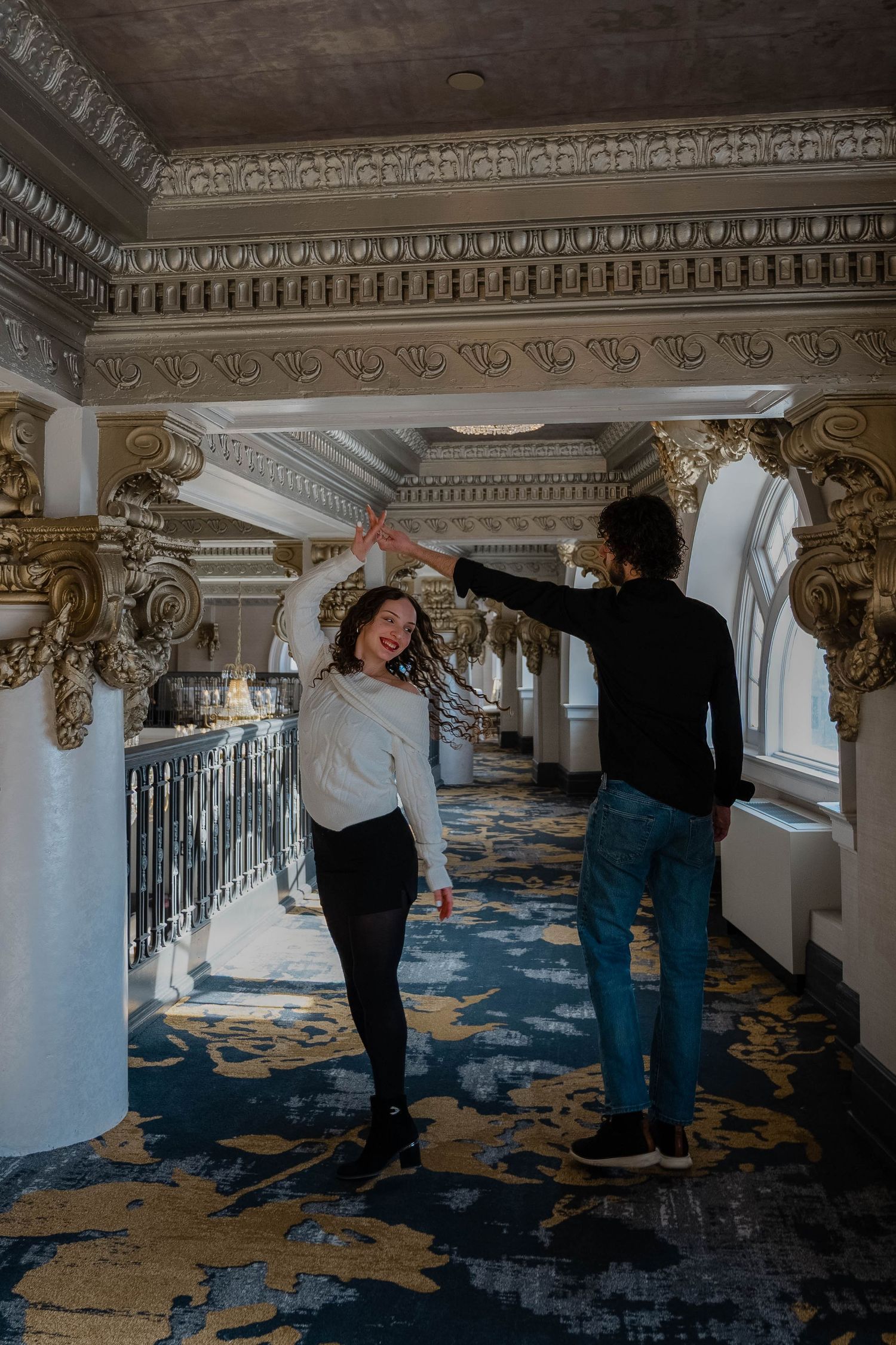 Couple dancing and spinning in a grand ornate hallway with gilded columns and decorative ceiling.