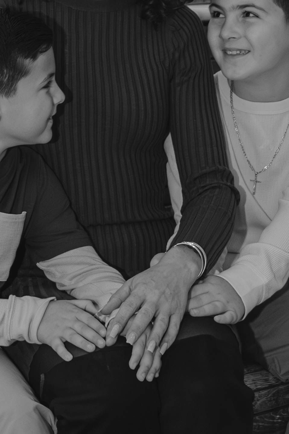 Black and white photo of a mother and two boys holding hands together indoors affectionately.