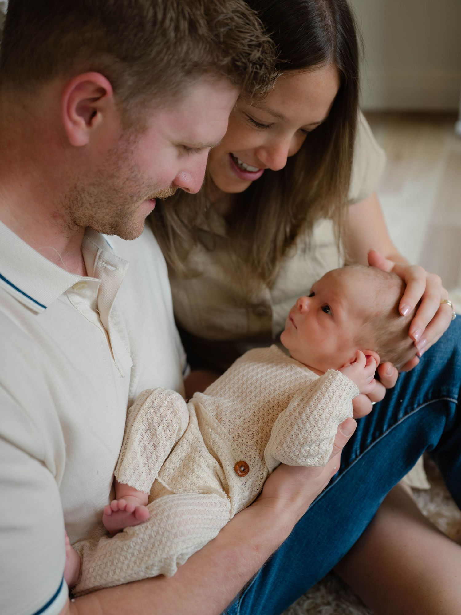 A couple smiles lovingly at their newborn baby, cradled gently in the father's arms during a warm family portrait.