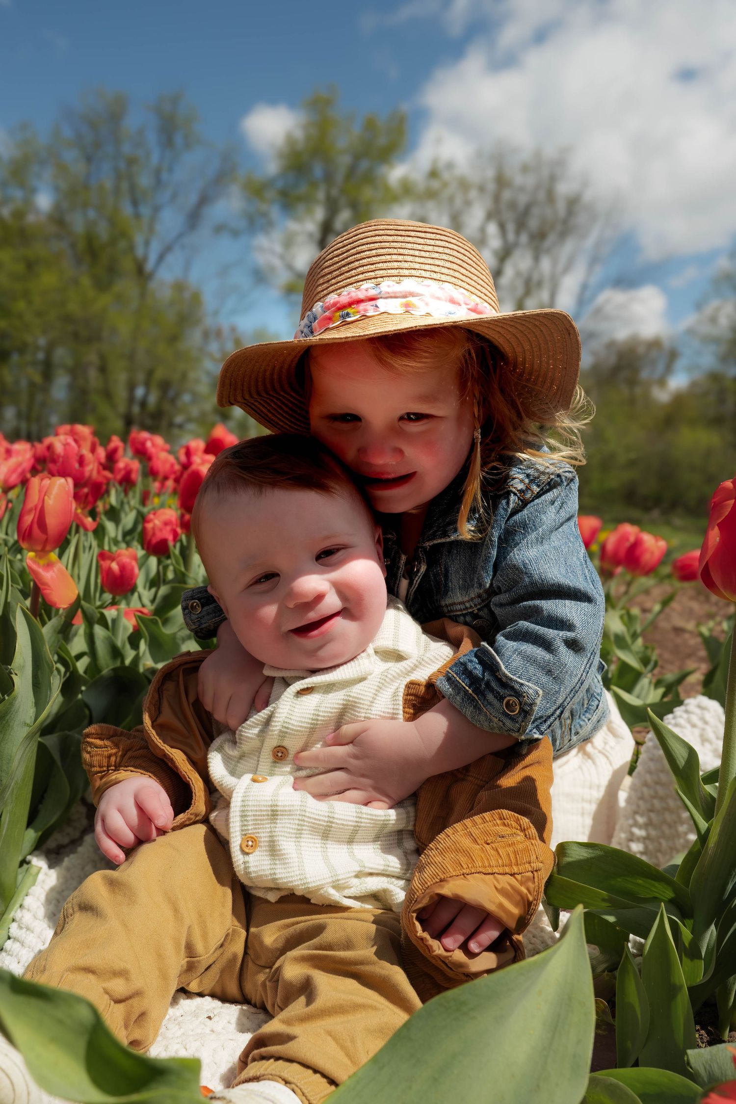 Adorable siblings posing together in a blooming red tulip field, baby smiling.