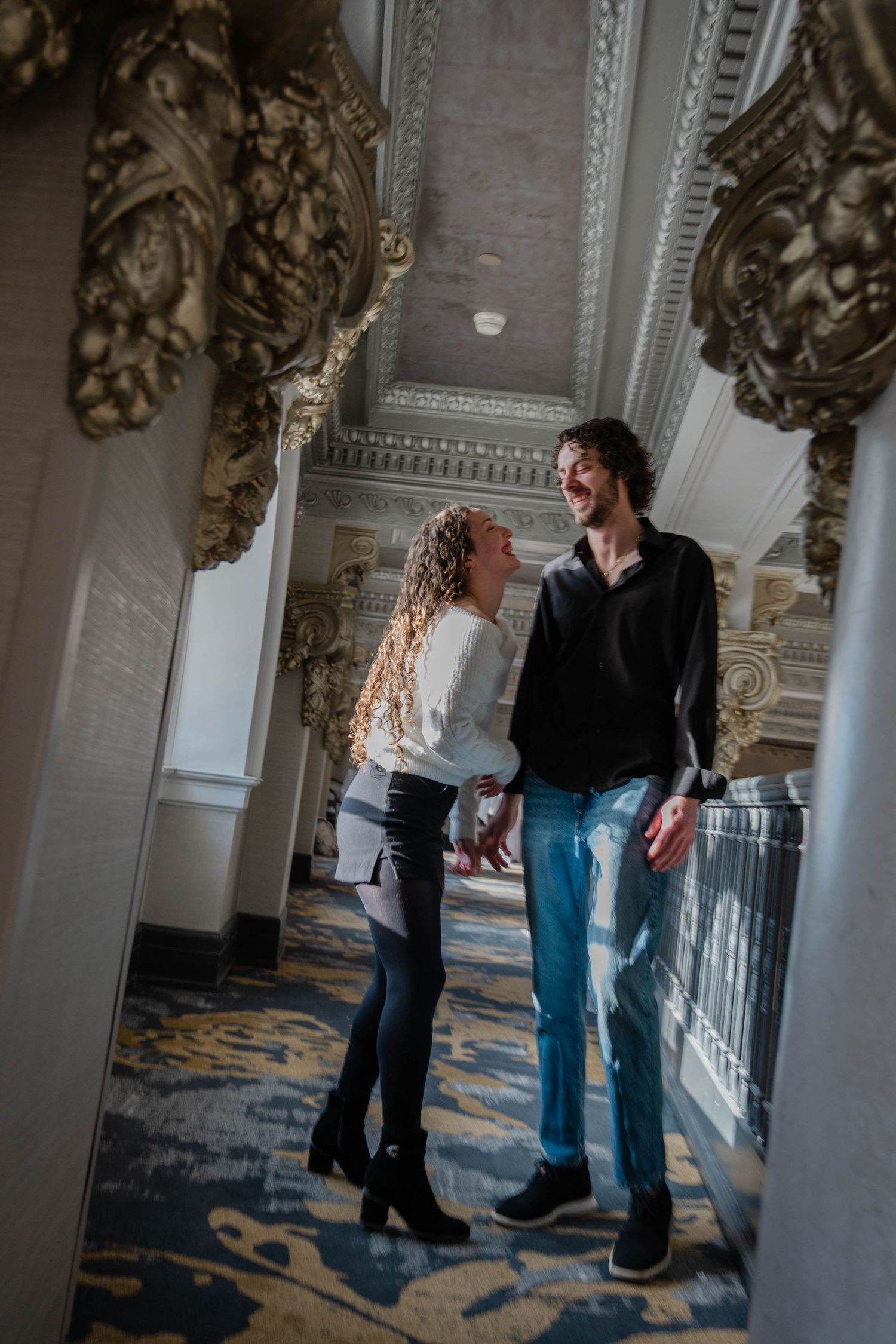 Smiling couple holding hands in a beautifully decorated hallway with baroque gold architectural elements.