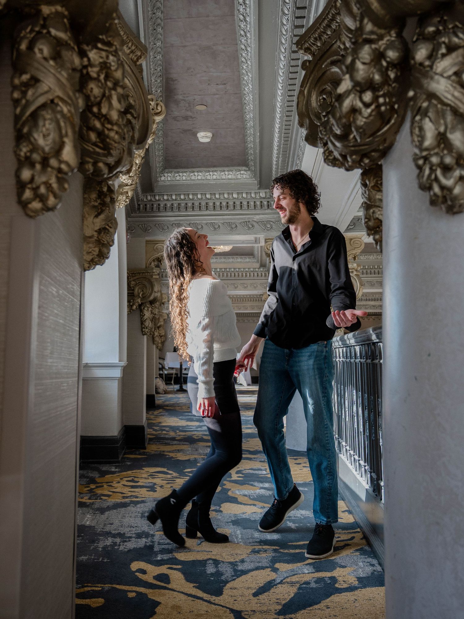 Couple laughing together in an elegant corridor with ornate gold architectural details and patterned carpet.