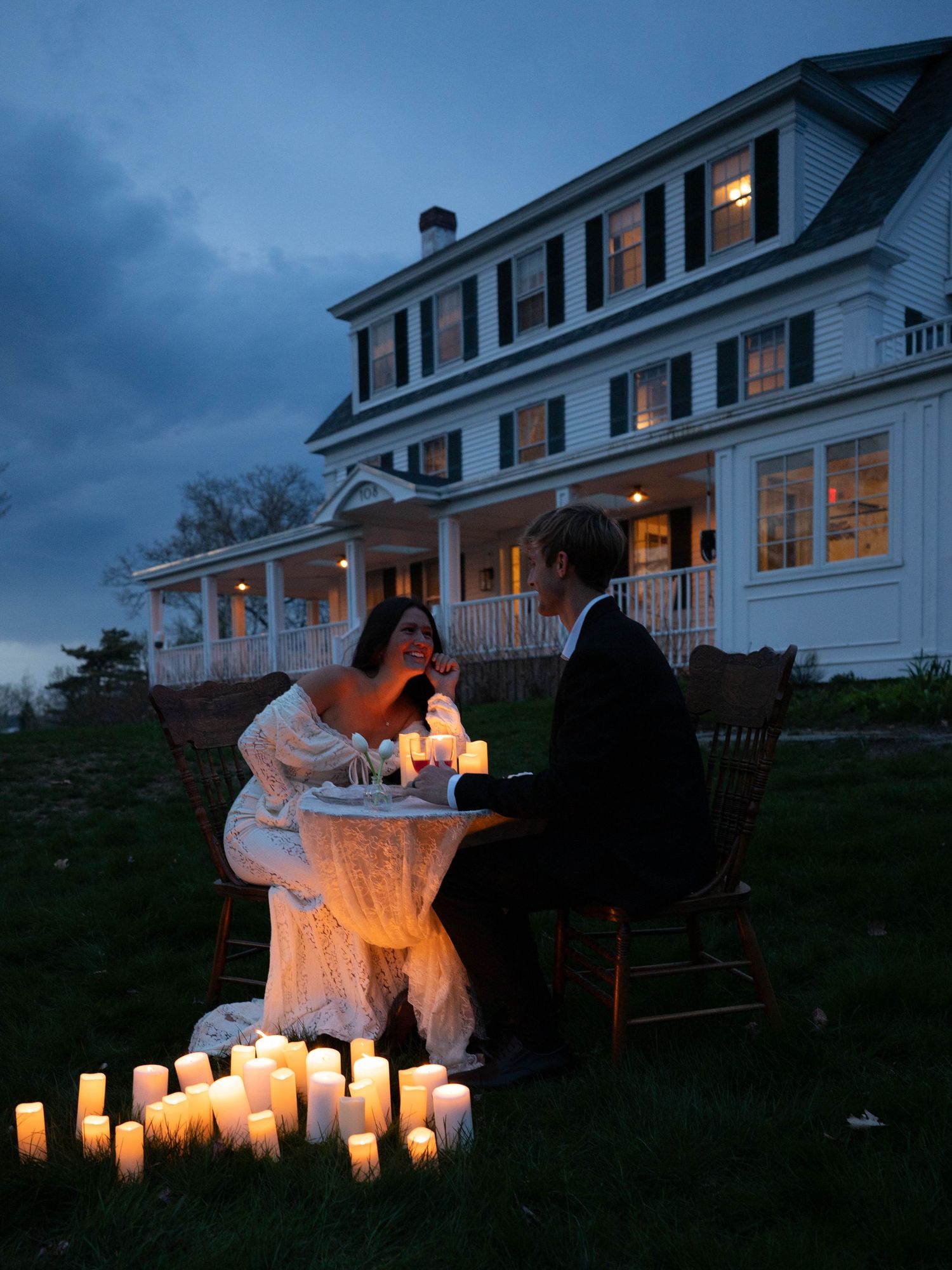 Romantic couple enjoying candlelit outdoor dinner at twilight surrounded by glowing white candles.