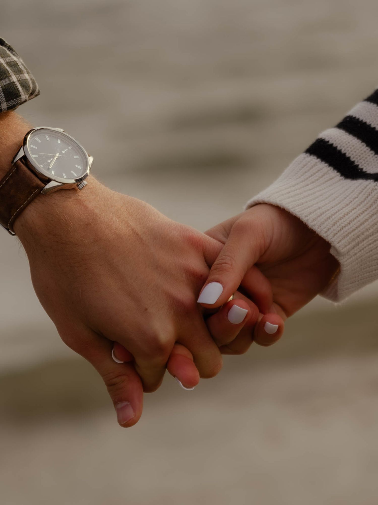 Close-up of a couple holding hands, man wearing a brown leather watch, woman with white manicure.