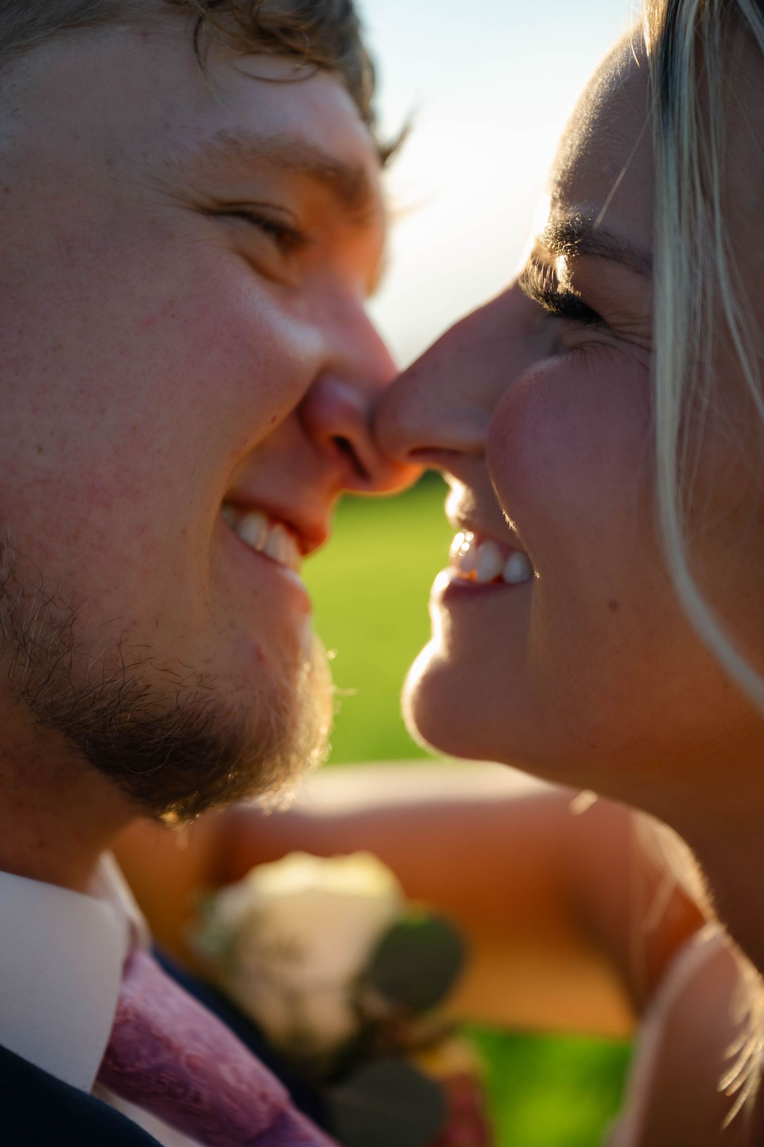 Close-up of smiling bride and groom sharing a romantic nose-to-nose moment outdoors on their wedding day.