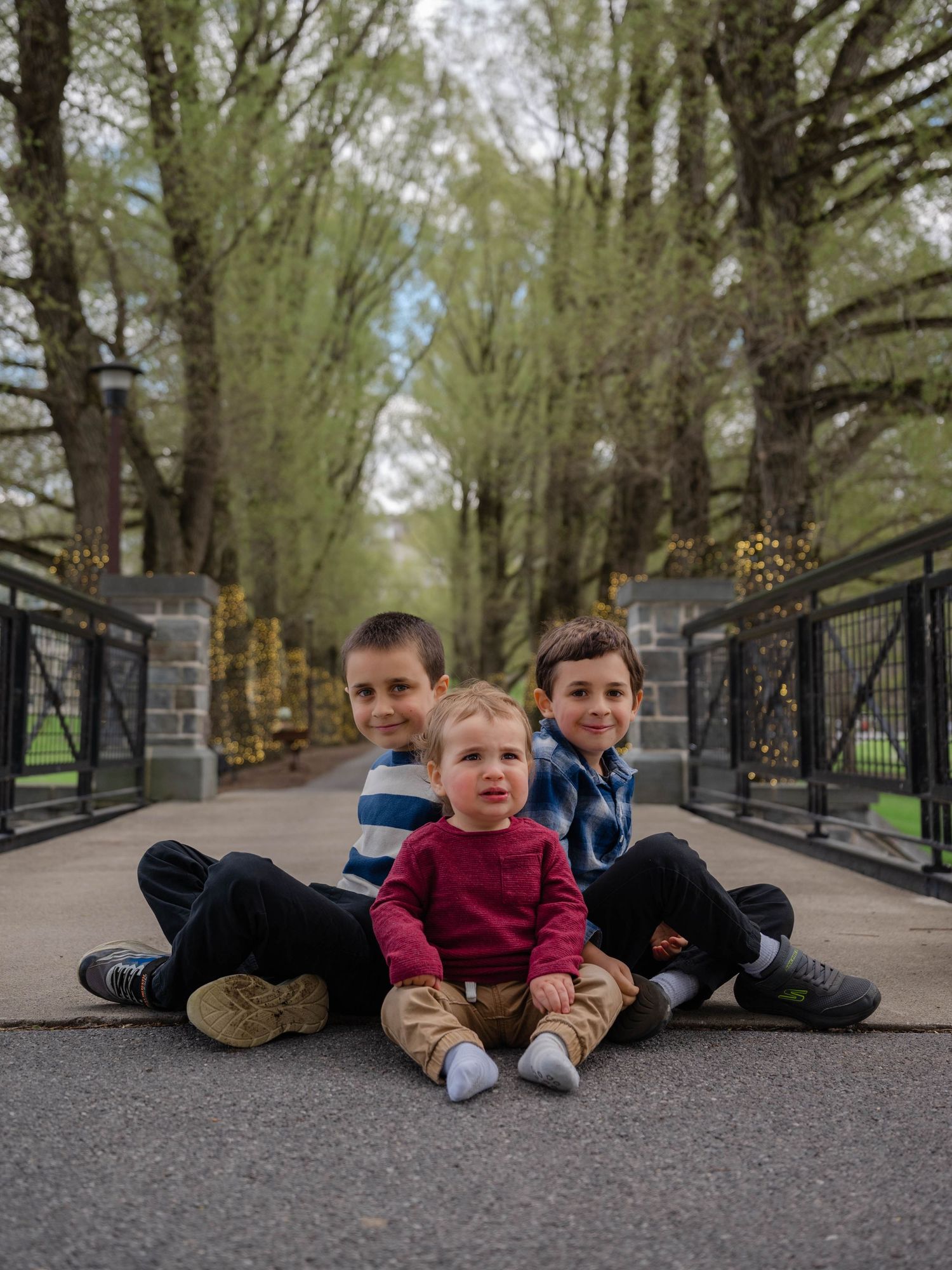 Three young brothers sitting together on a bridge path surrounded by spring trees in park. Hamilton New York Colgate college