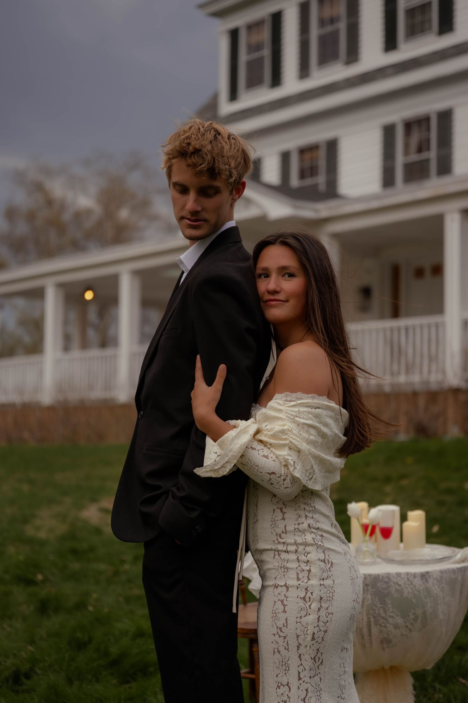 Elegant couple in wedding attire pose together at twilight near a candlelit outdoor table.