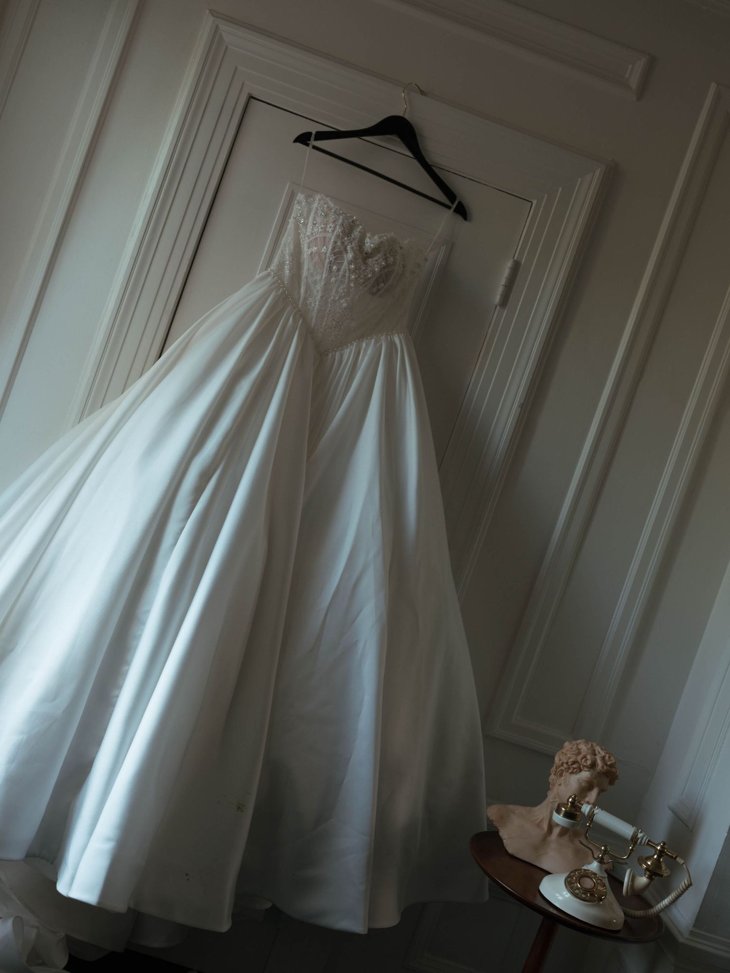 Elegant strapless ball gown wedding dress hanging on a door in a softly lit bridal suite.