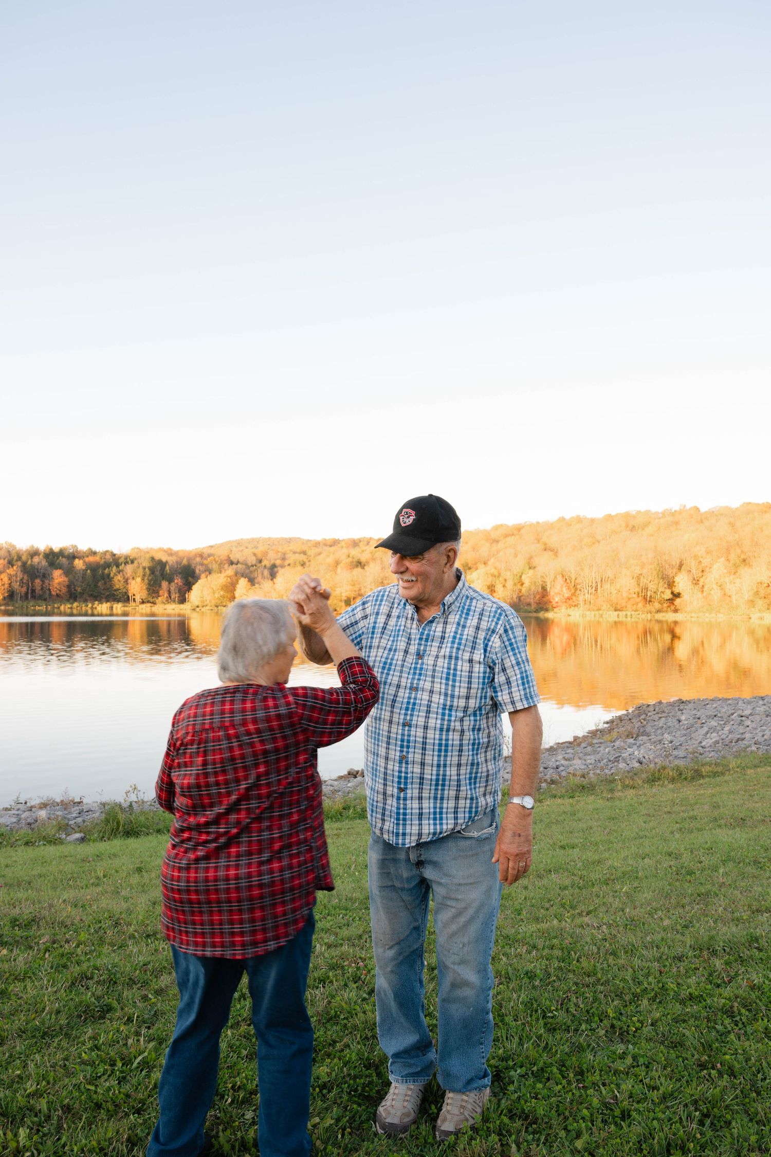 Senior couple dancing and holding hands by a beautiful fall foliage lake at sunset. Central New York