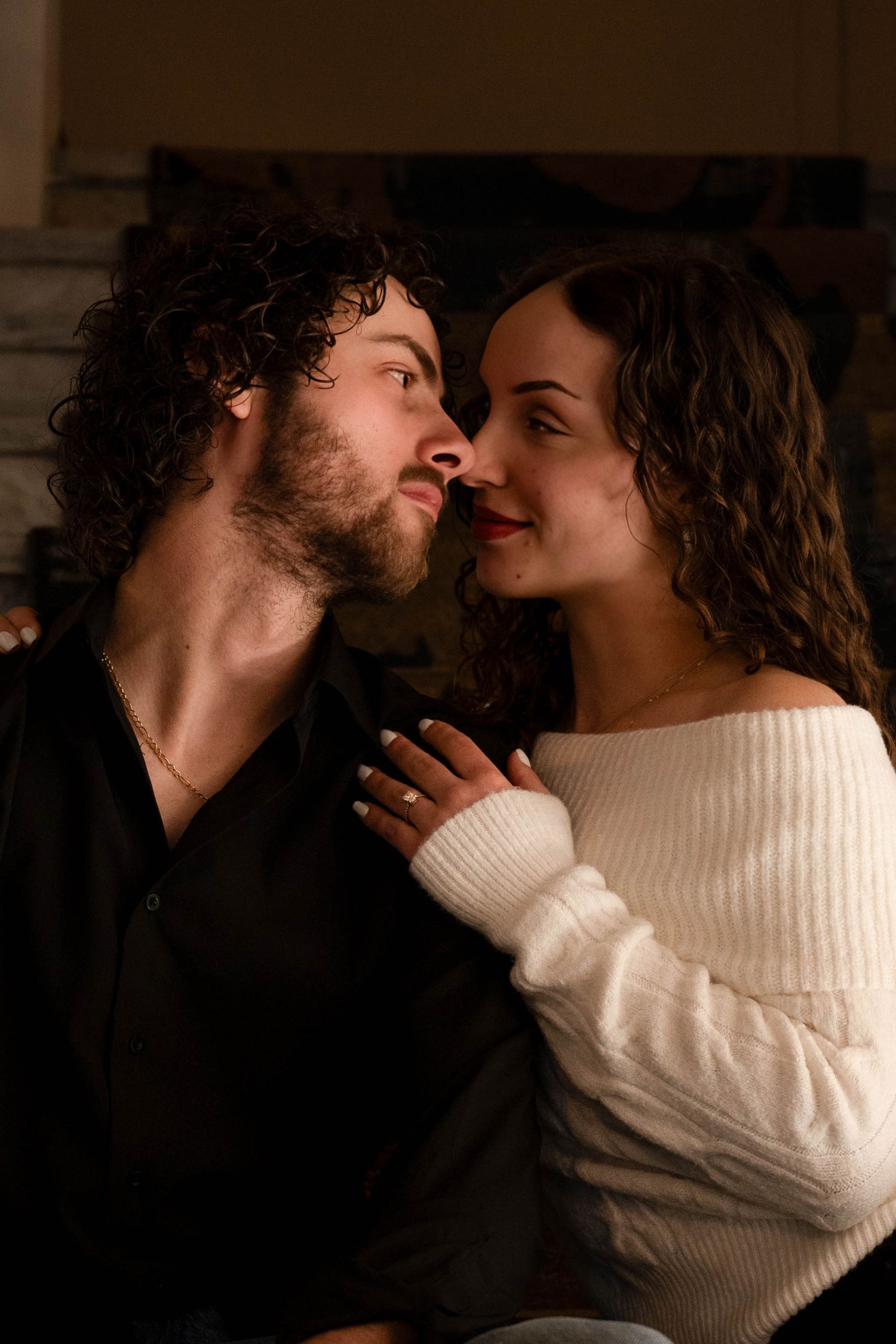 A romantic couple gazes into each other's eyes while sharing an intimate moment by a fireplace.