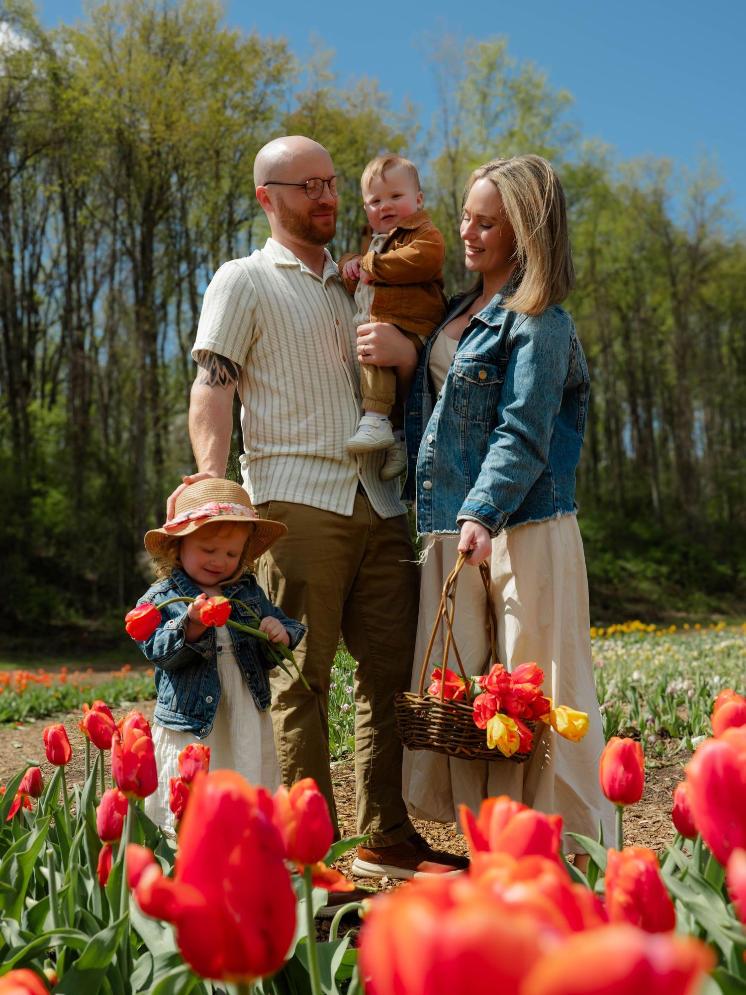 Family of four poses in vibrant red tulip field on sunny spring day.