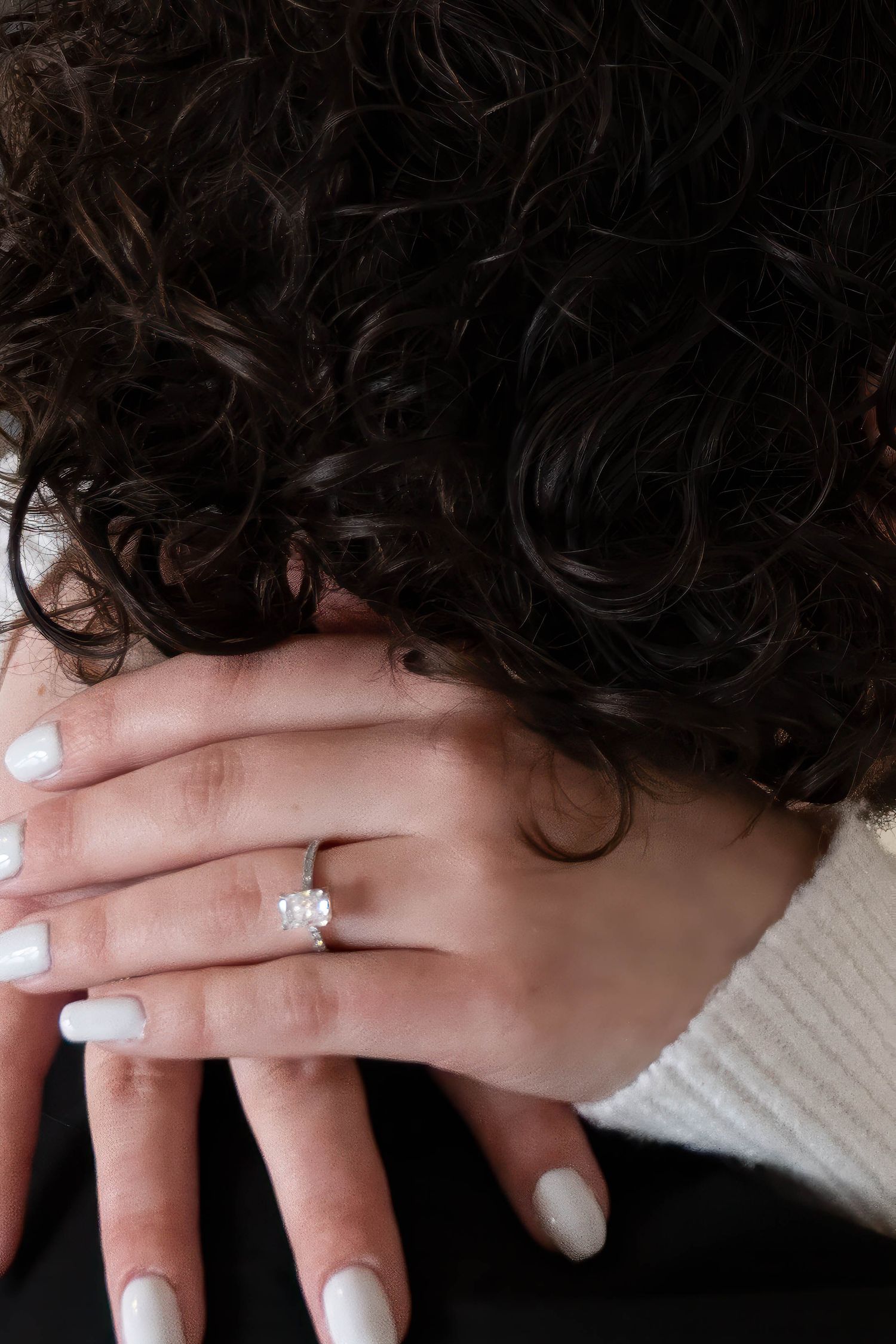 Close-up of an engagement ring with a diamond cluster setting on a womans hand with white nails.