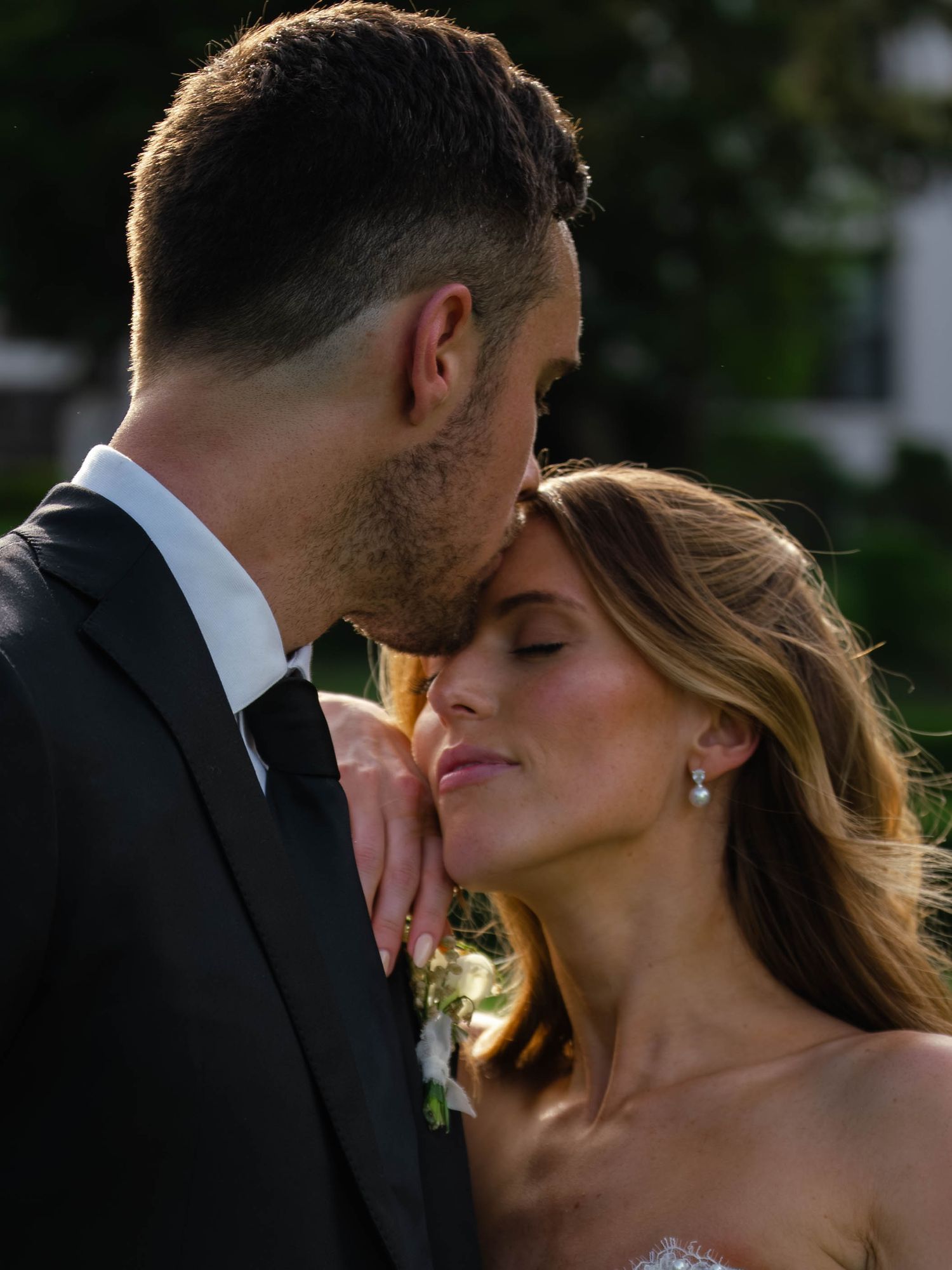 Groom gently cradles bride's face in golden hour light during intimate outdoor wedding portrait session.