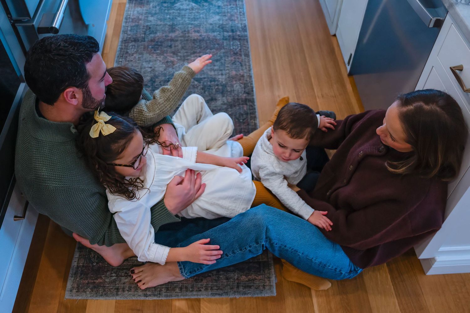 Aerial view of a happy family of five sitting together on a hardwood floor, laughing and playing.