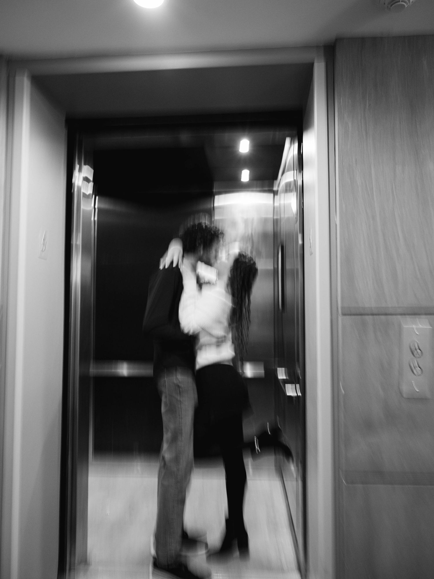 Blurry black and white photo of couple embracing in an elevator doorway.
