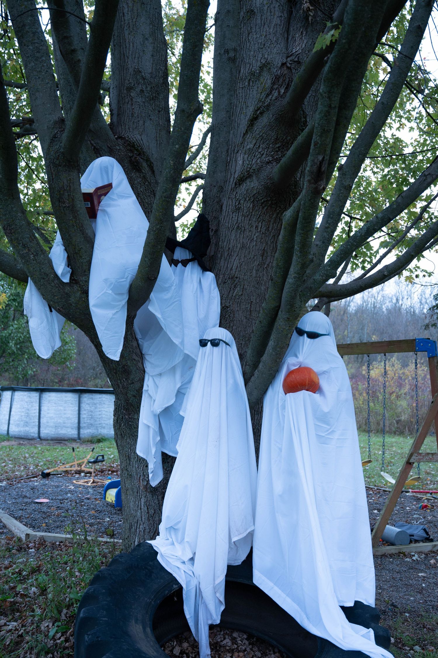 Three Halloween ghost decorations made from white sheets hanging on a tree in an outdoor yard display.