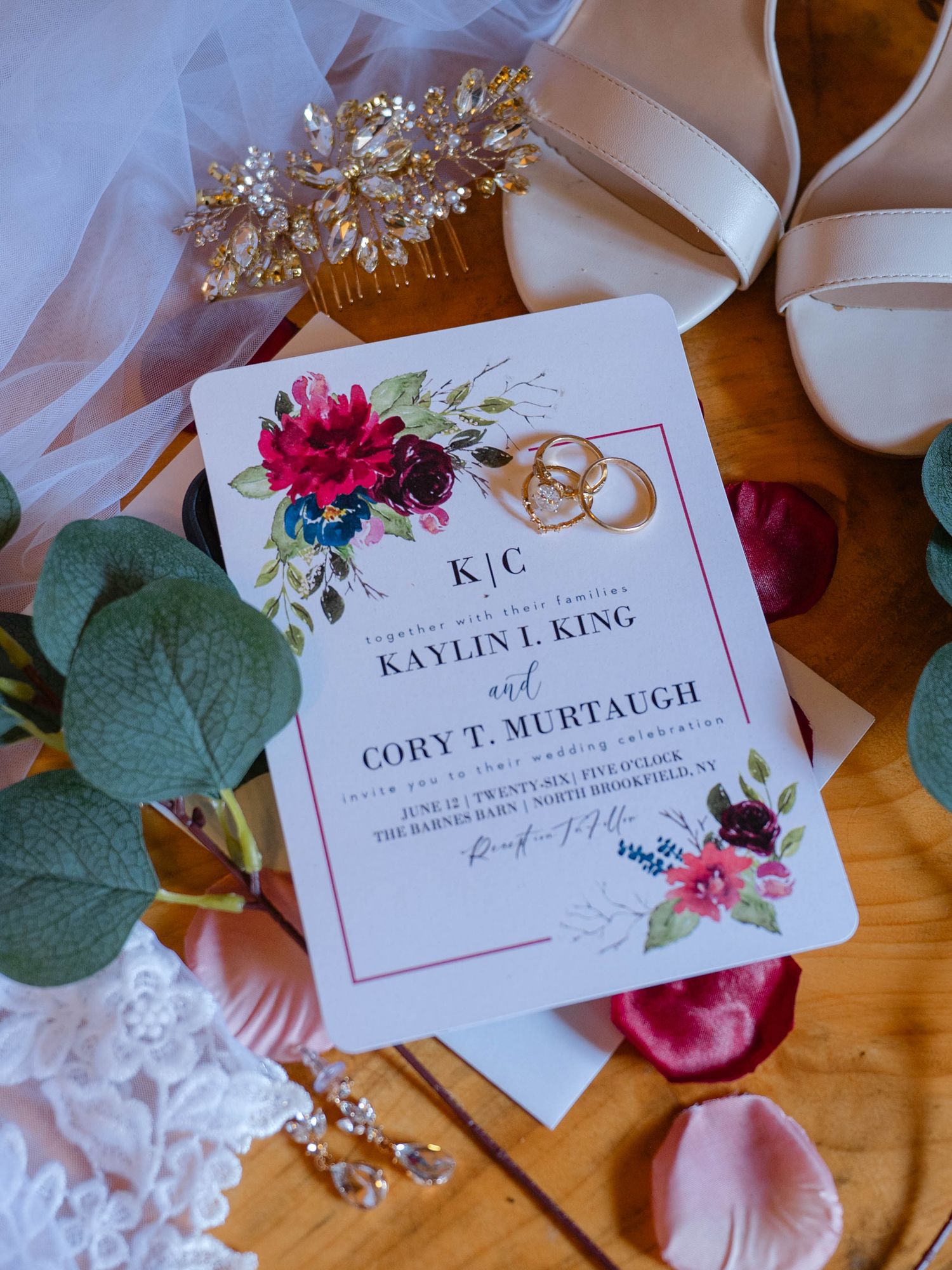 Elegant wedding invitation for Kaylin King and Cory Murtaugh with floral design, gold rings, bridal accessories on wooden surface.