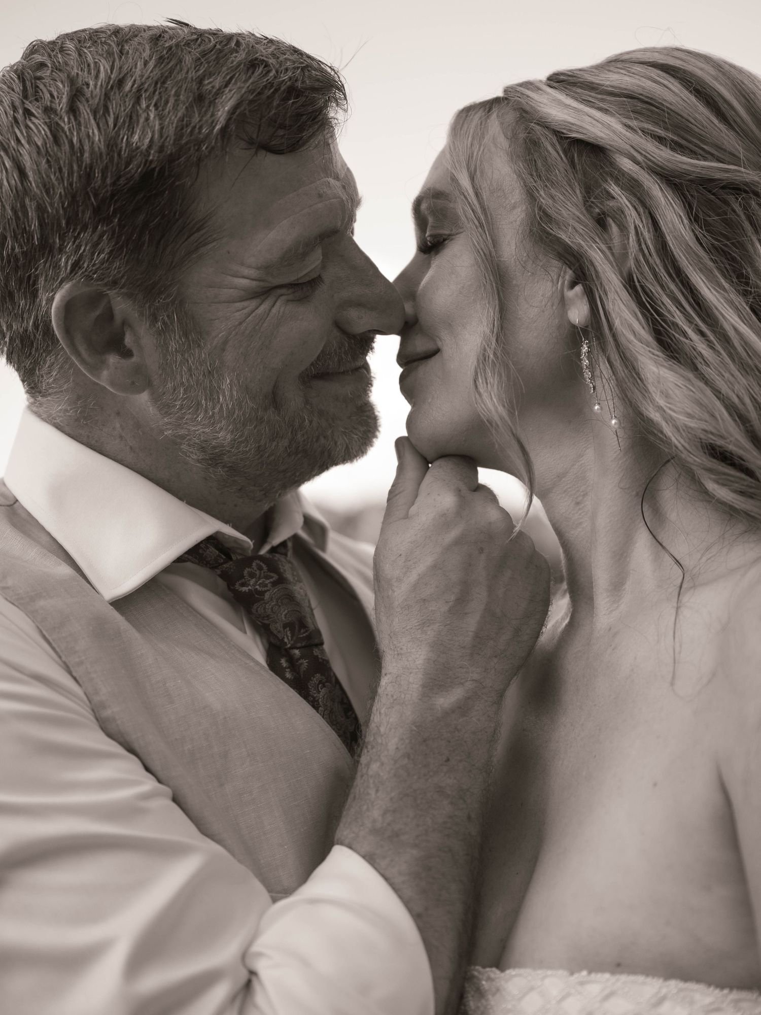 Black and white wedding photo of a couple sharing an intimate moment, the groom tenderly holding the bride's chin as they lean close.