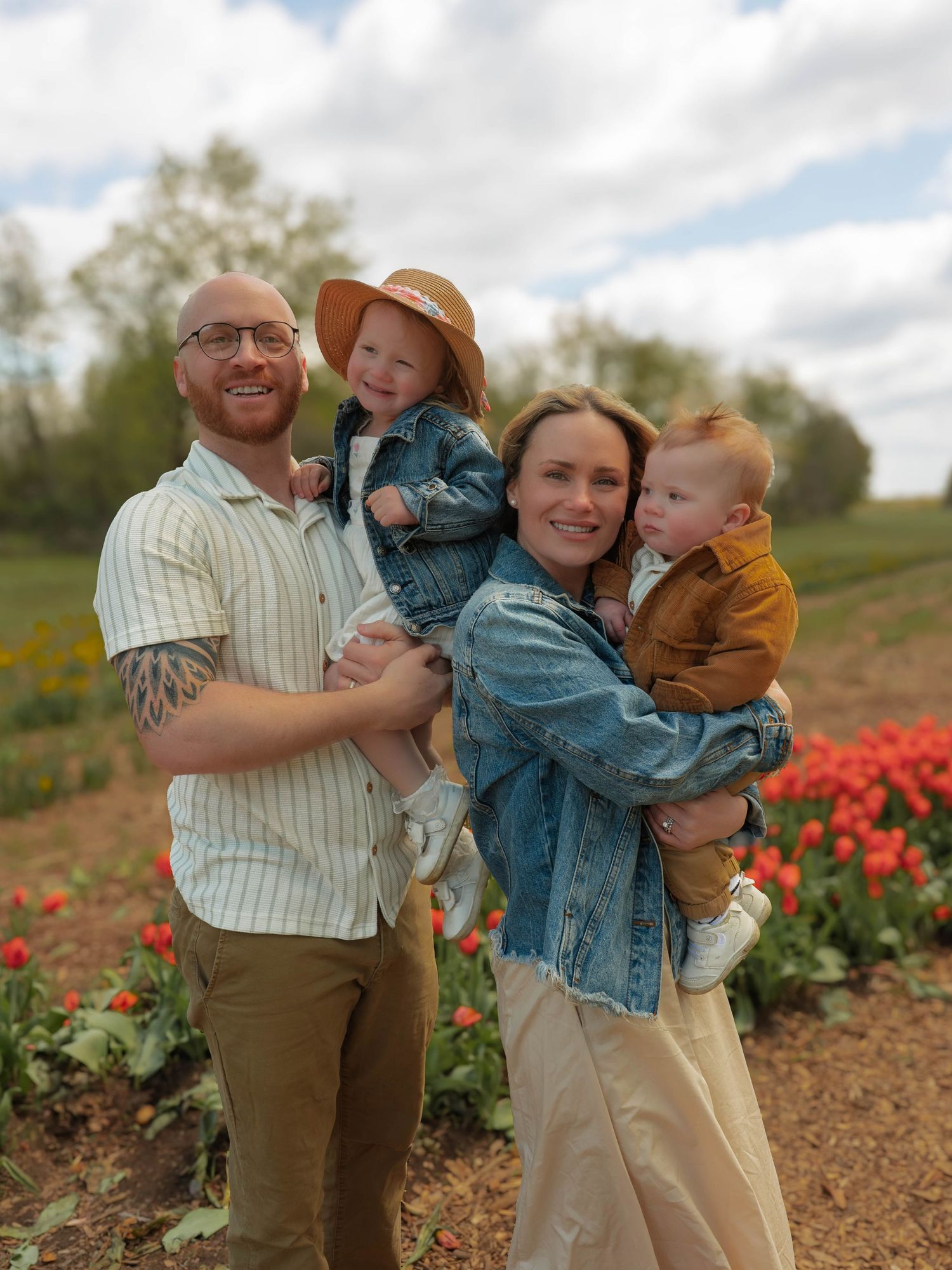Smiling family of four posing together in front of vibrant red tulip rows.