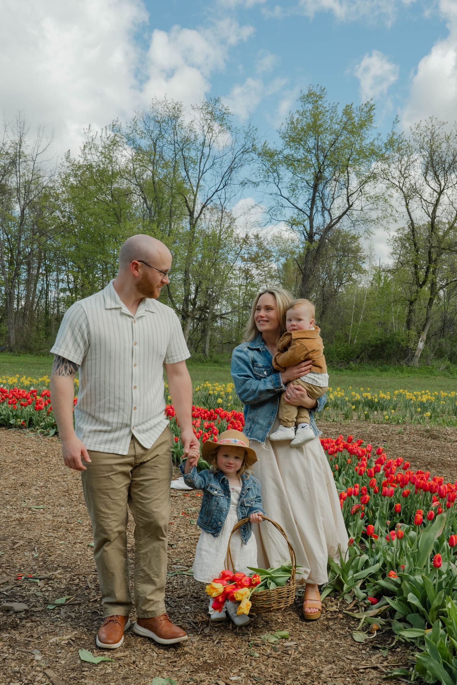 Family of four posing in colorful tulip field with basket of picked flowers on sunny day.