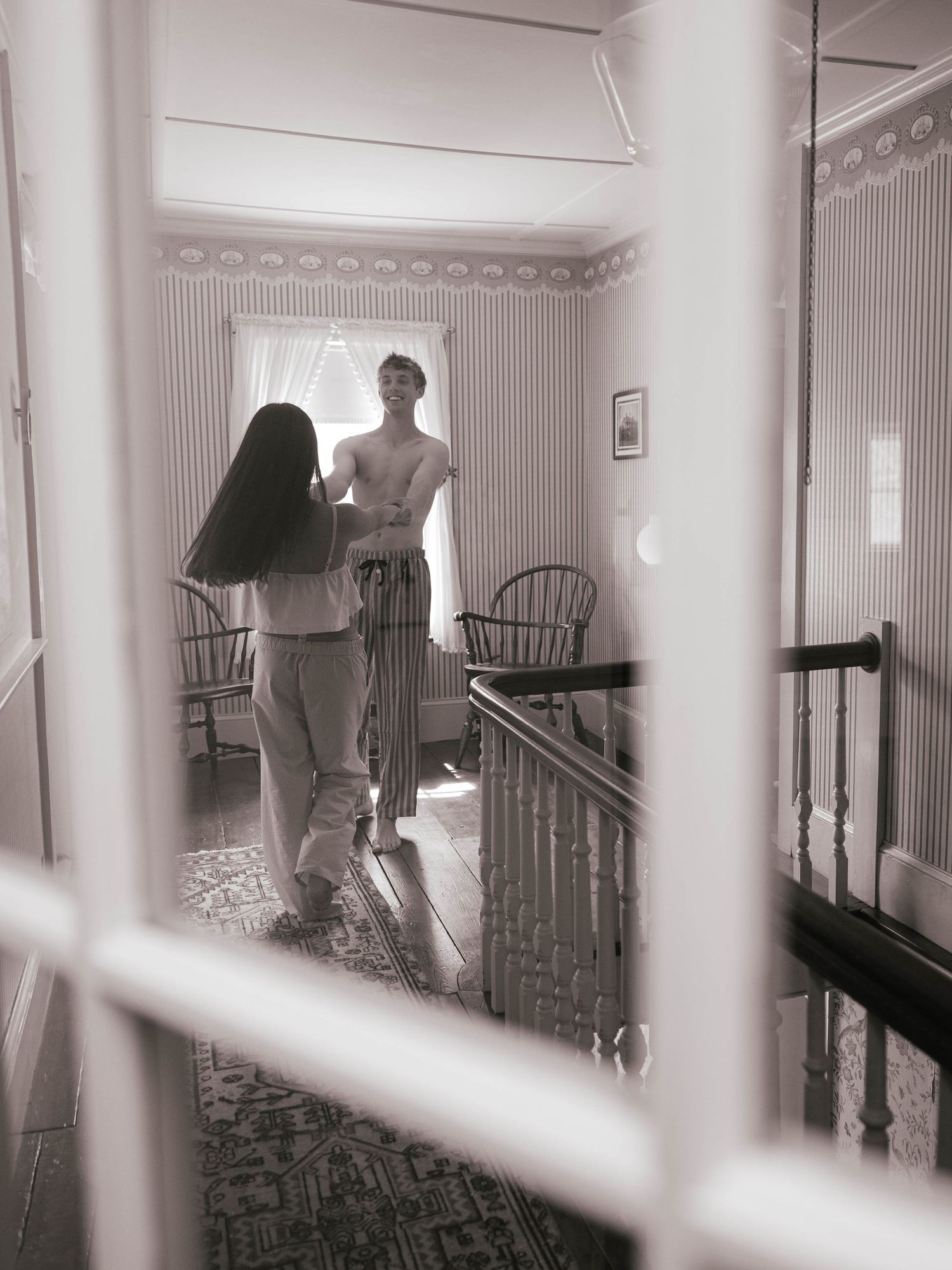 Black and white photo of a couple standing together near a staircase in a cozy home.