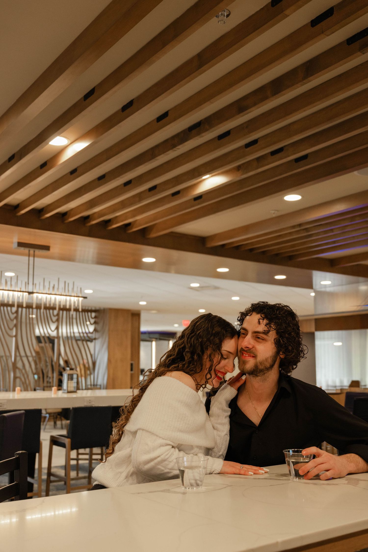 Couple sharing an intimate moment at a modern bar, woman leaning into mans shoulder.