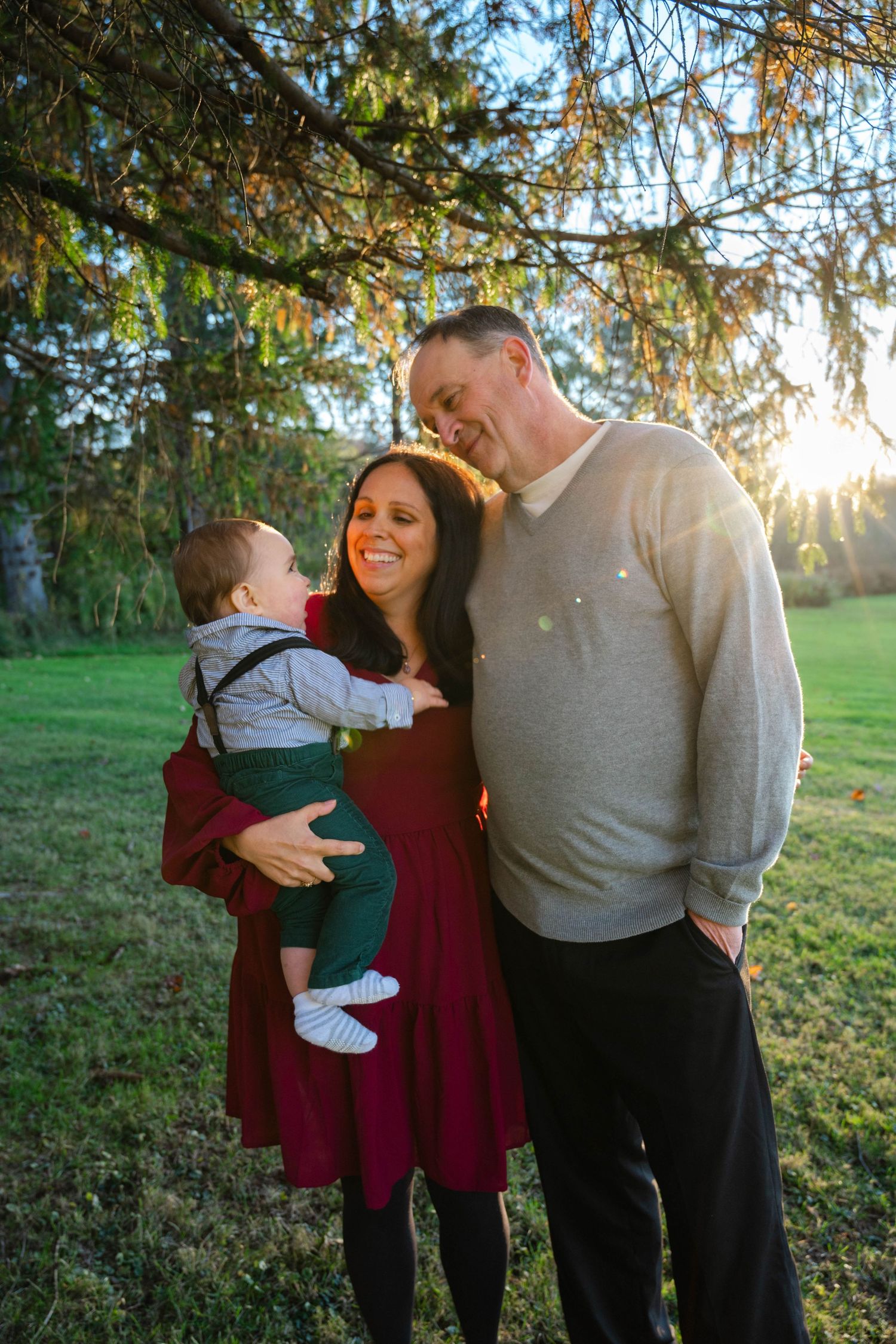 Happy couple sharing a joyful moment with their baby outdoors in warm sunset light.
