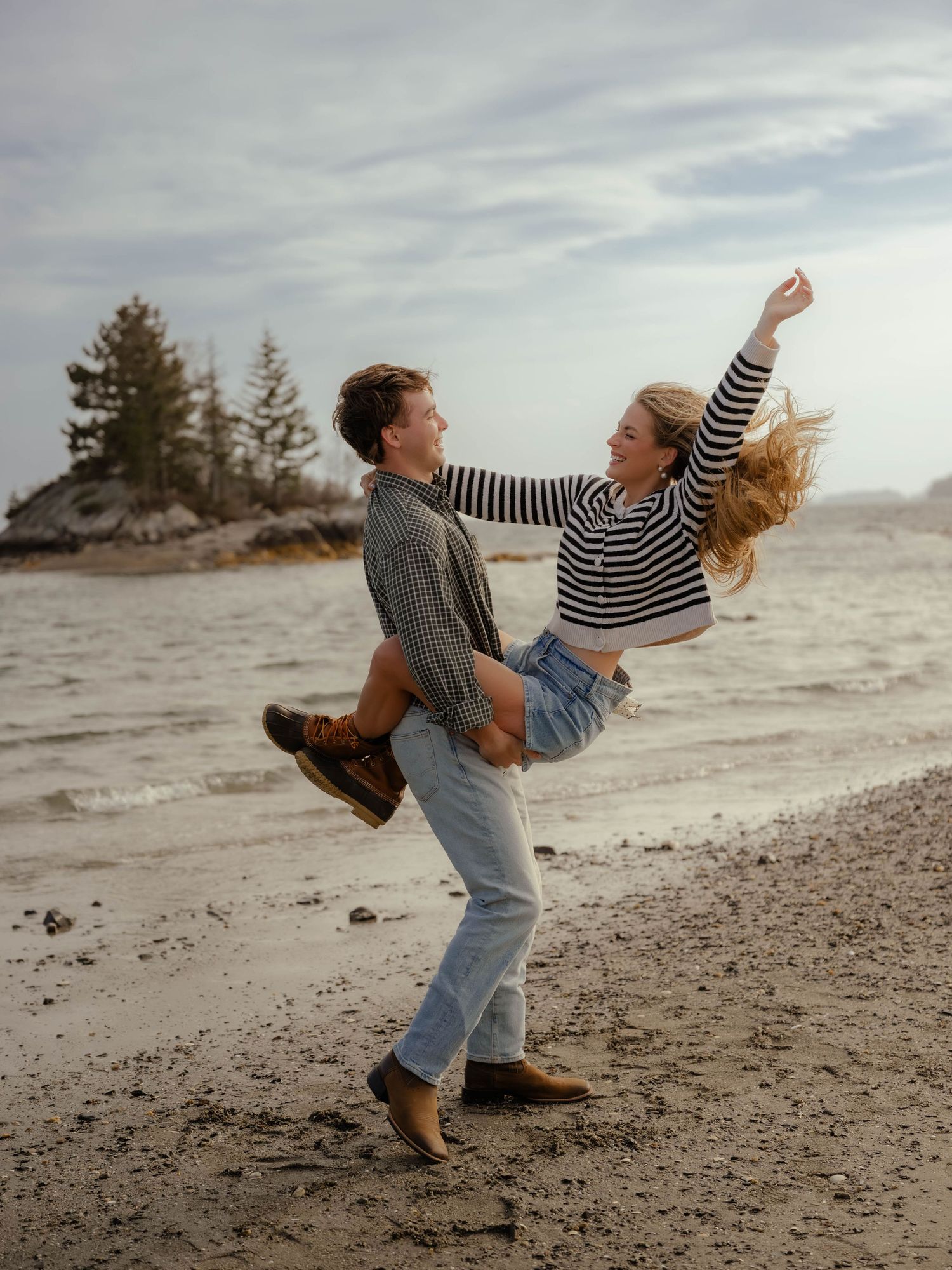 Joyful couple dancing on a sandy beach, woman being lifted and spinning by the shore.