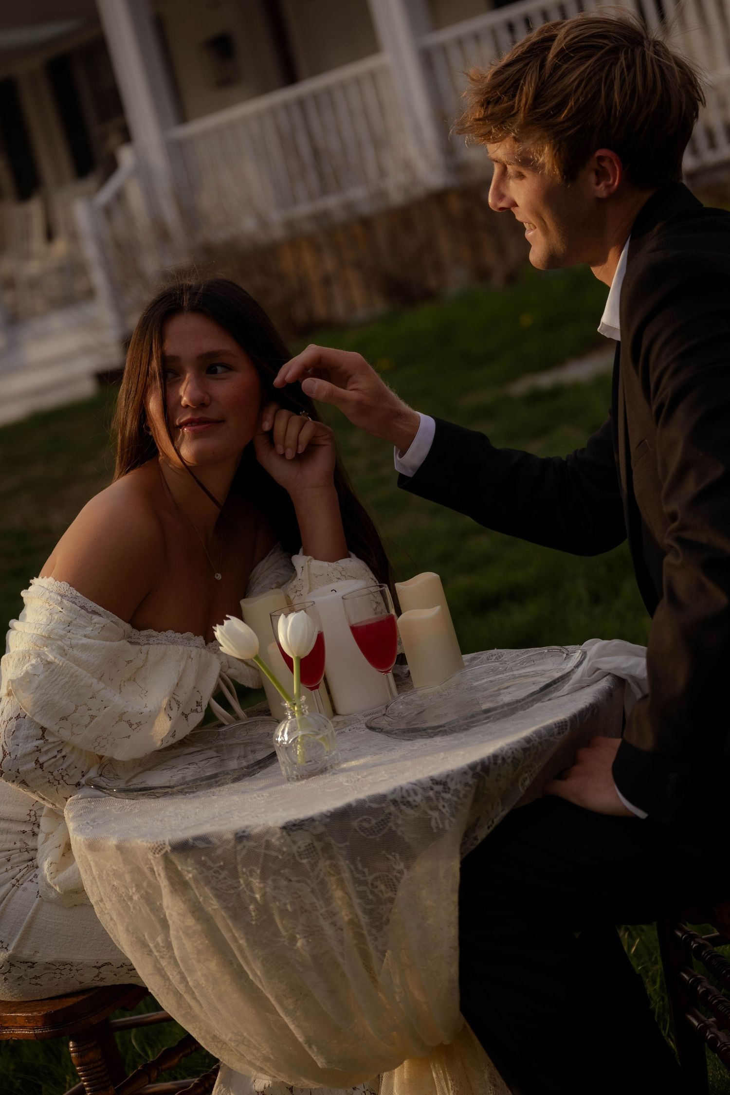 Groom tenderly touches bride's hair as she gazes up at him at candlelit outdoor table.