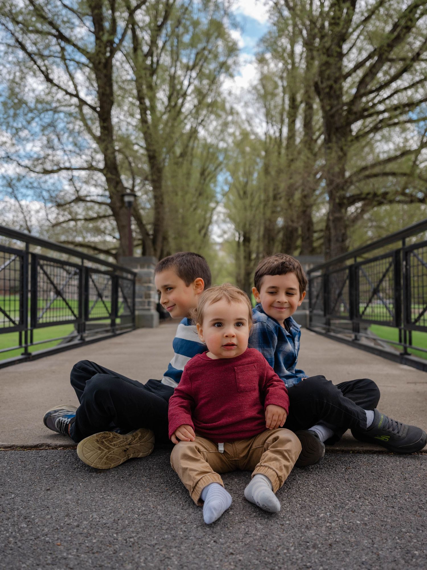 Three brothers posing on a bridge walkway with tall spring trees lining the path behind them.Hamilton New York Colgate college