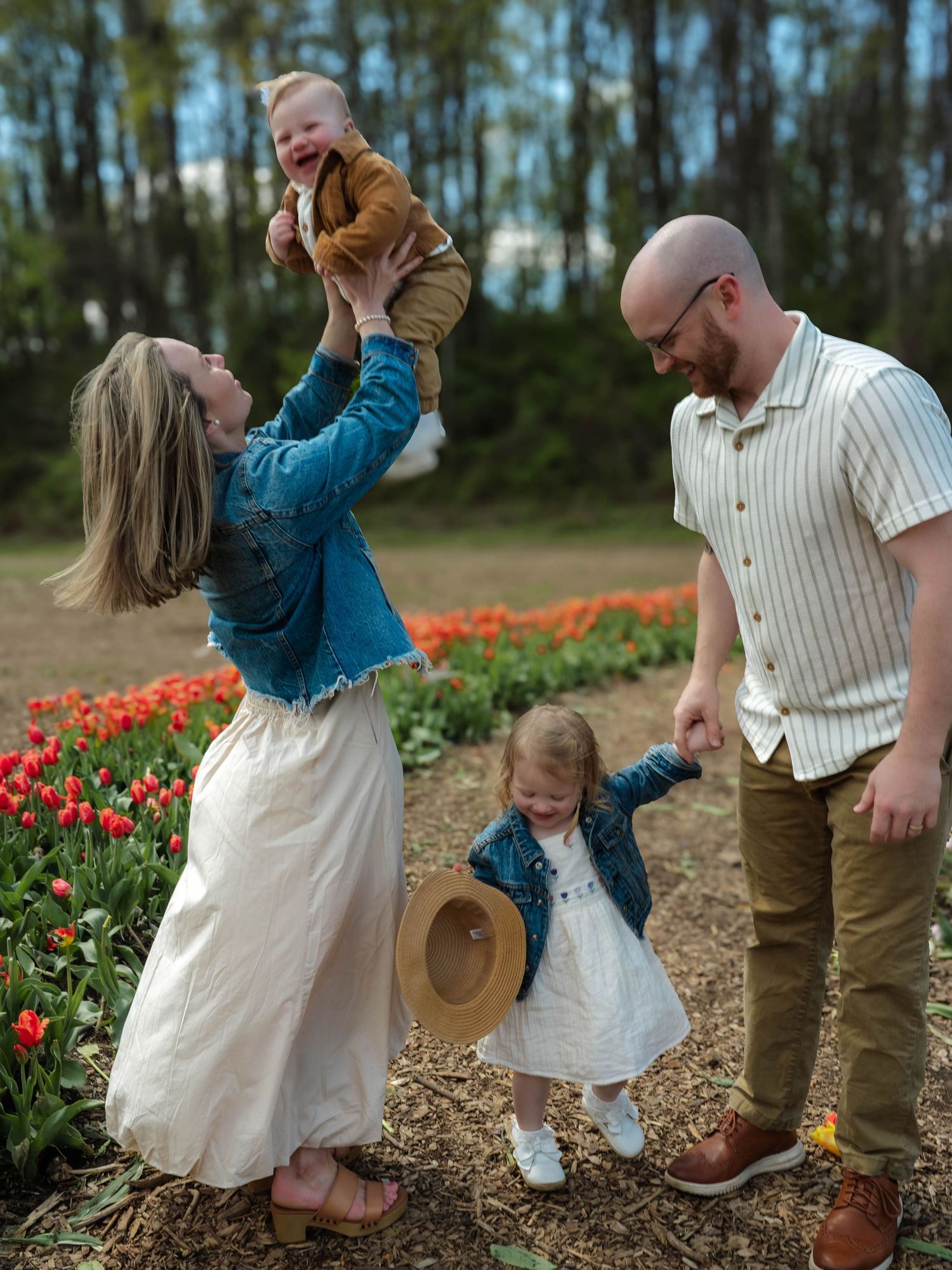 Happy family of four playing together near colorful tulip garden in spring.