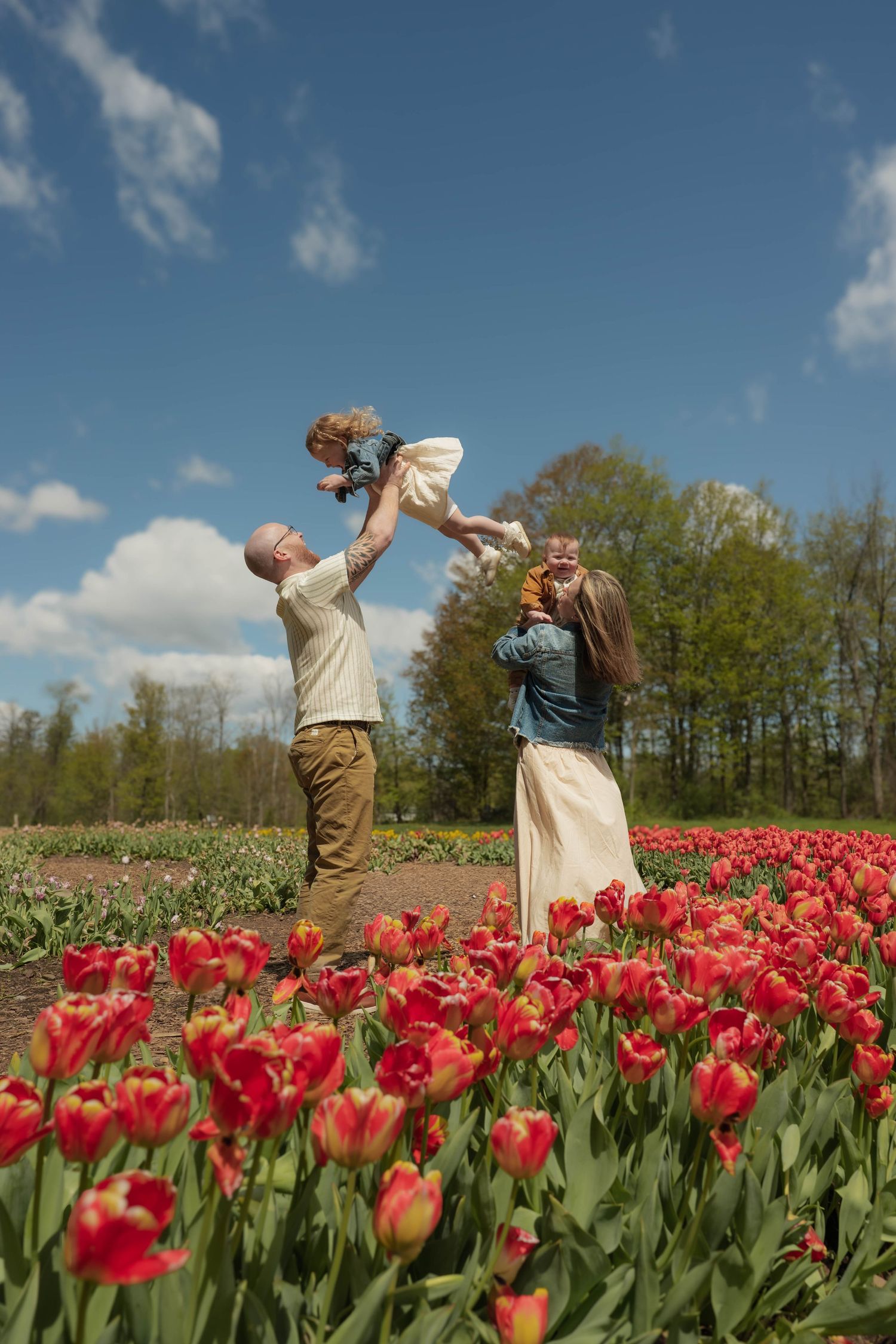 Joyful parents tossing children in the air among red tulips under blue sky.