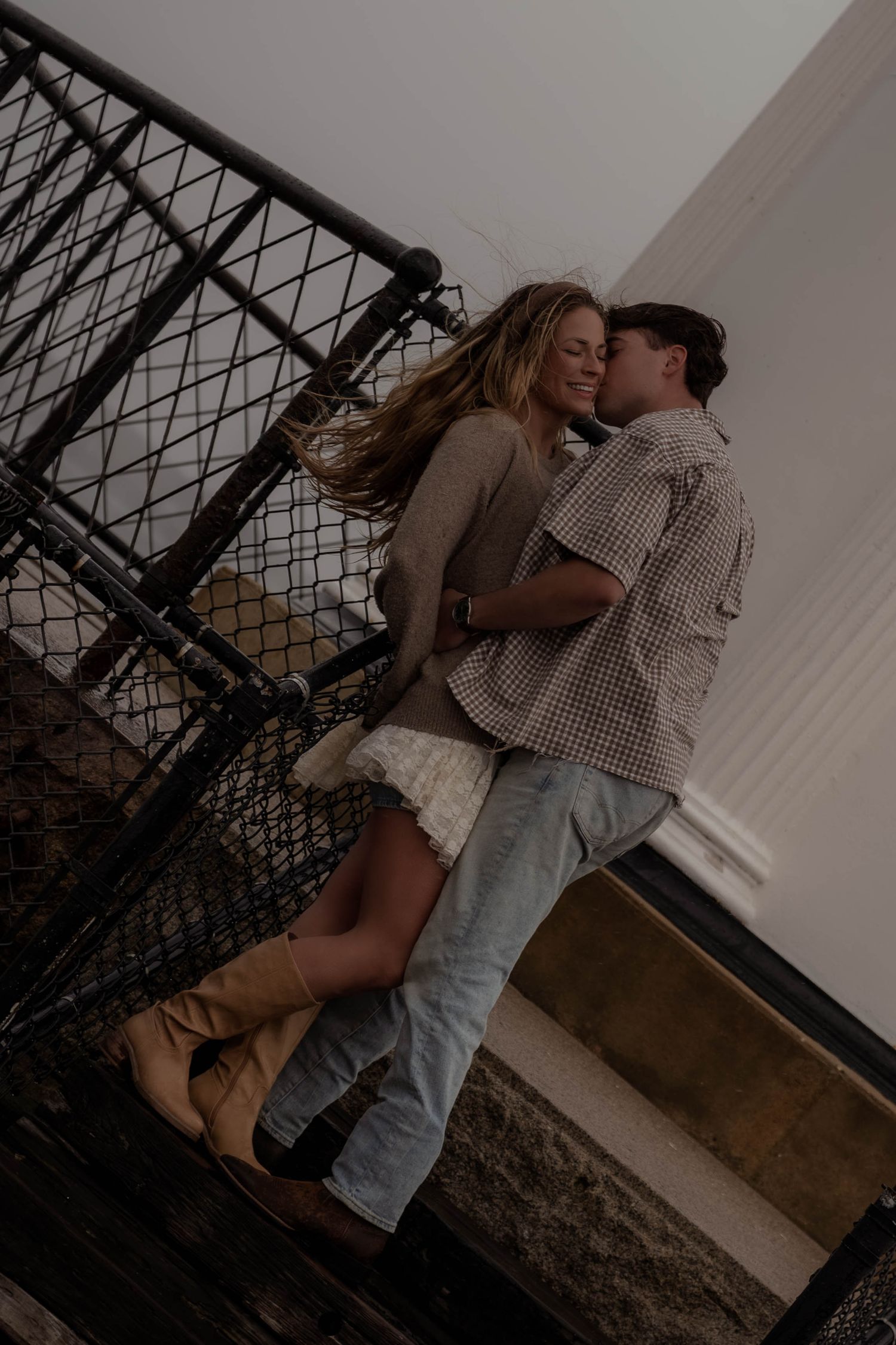 Couple embracing and laughing together on metal walkway near lighthouse.