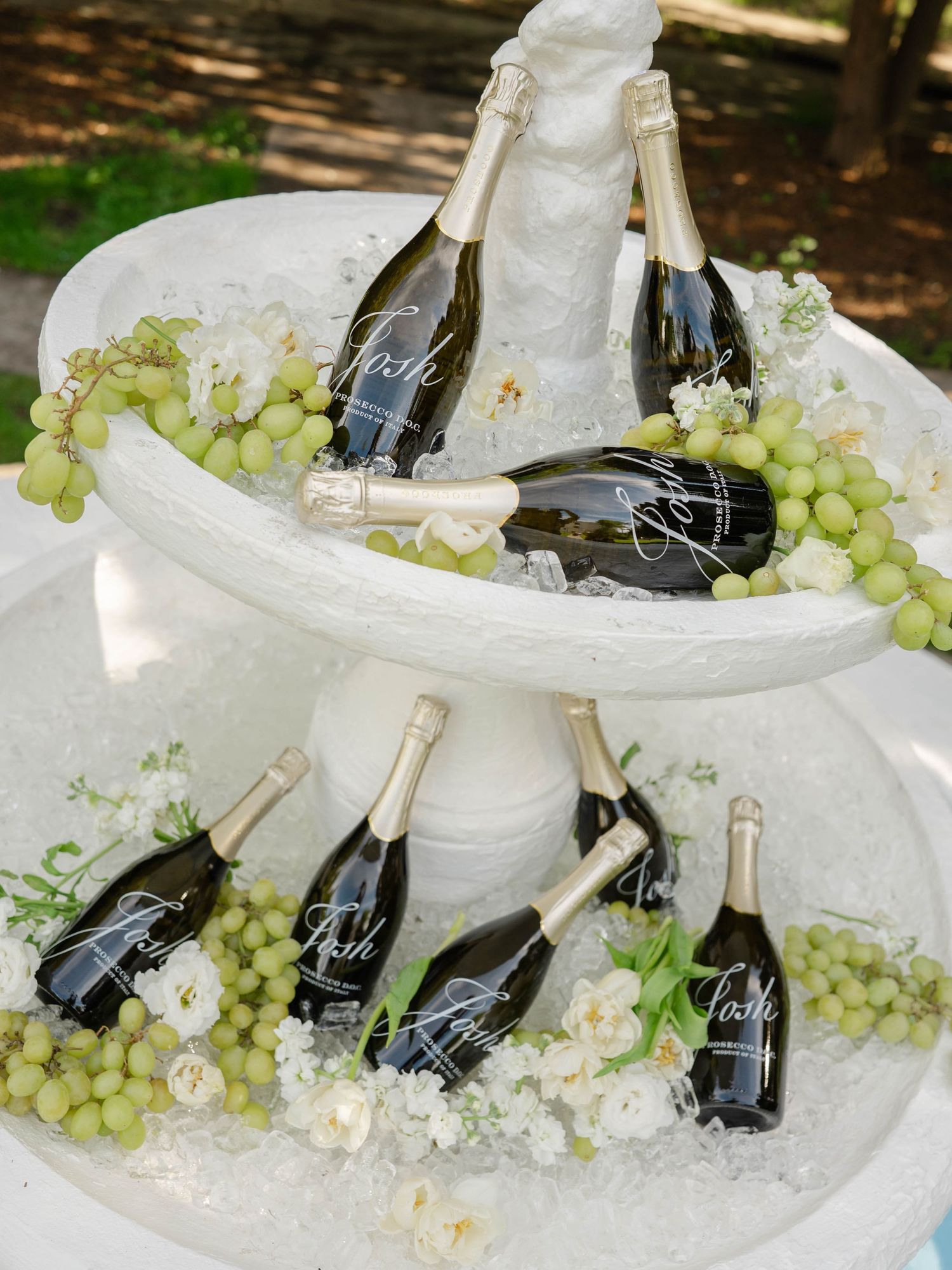 Chilled champagne bottles with custom labels displayed on tiered ice fountain with green grapes.