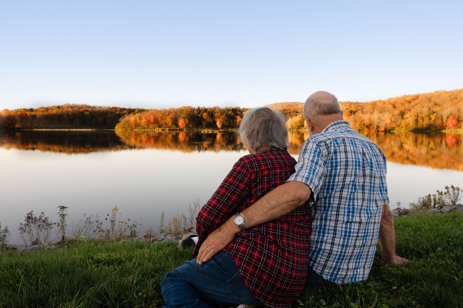 Senior couple sitting close together overlooking a peaceful lake surrounded by autumn colored trees.